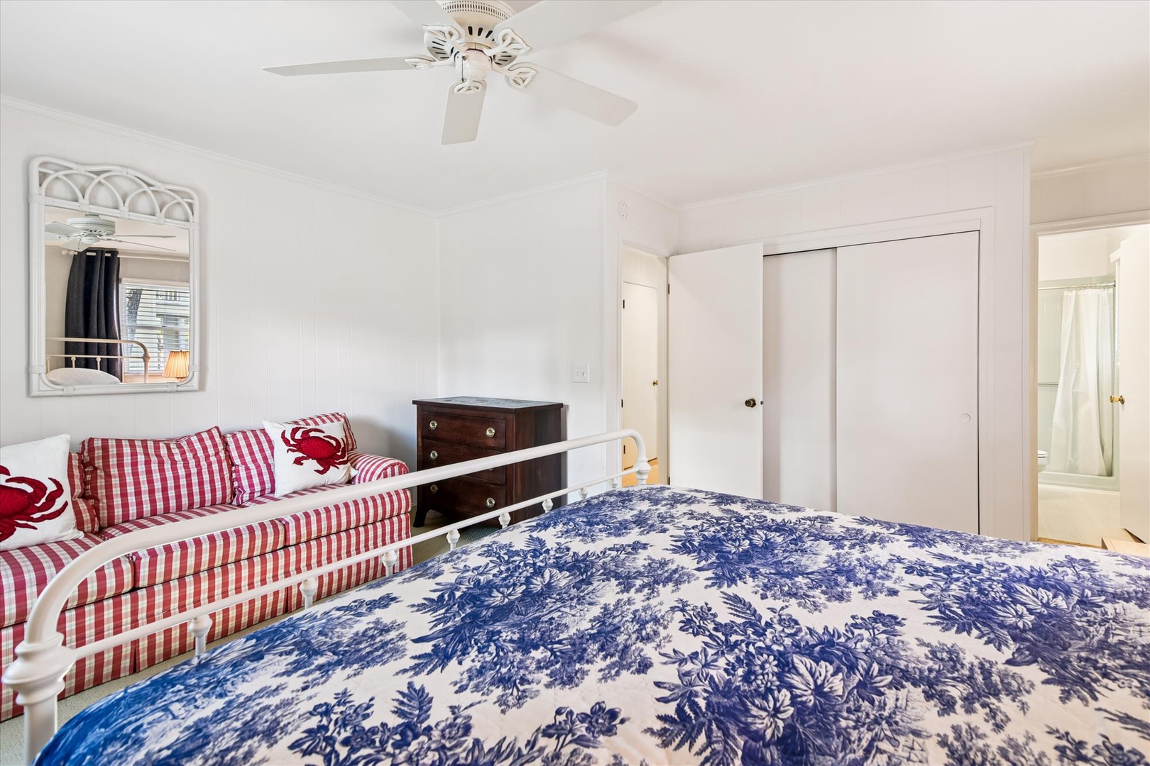 Drift off to sleep in this charming bedroom featuring a plush bed with blue floral linens and cozy red gingham seating area.