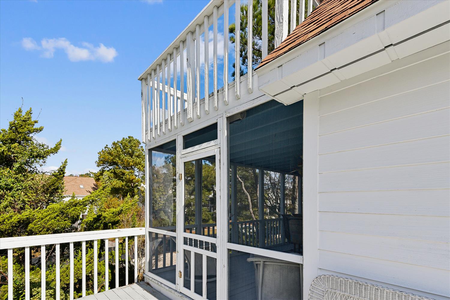 White cottage exterior showcases charming balcony and screened porch area surrounded by lush neighborhood greenery.