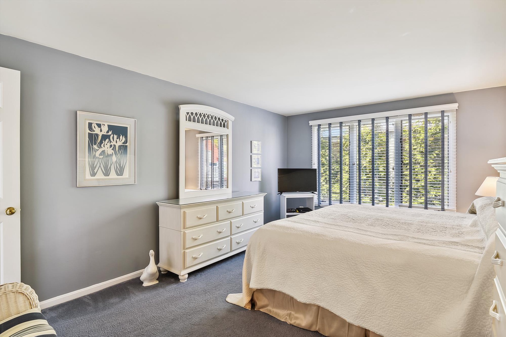 Relax in your serene bedroom with soft natural light filtering through plantation shutters, highlighting elegant white furnishings and calming coastal décor perfect for peaceful mornings and restful nights.