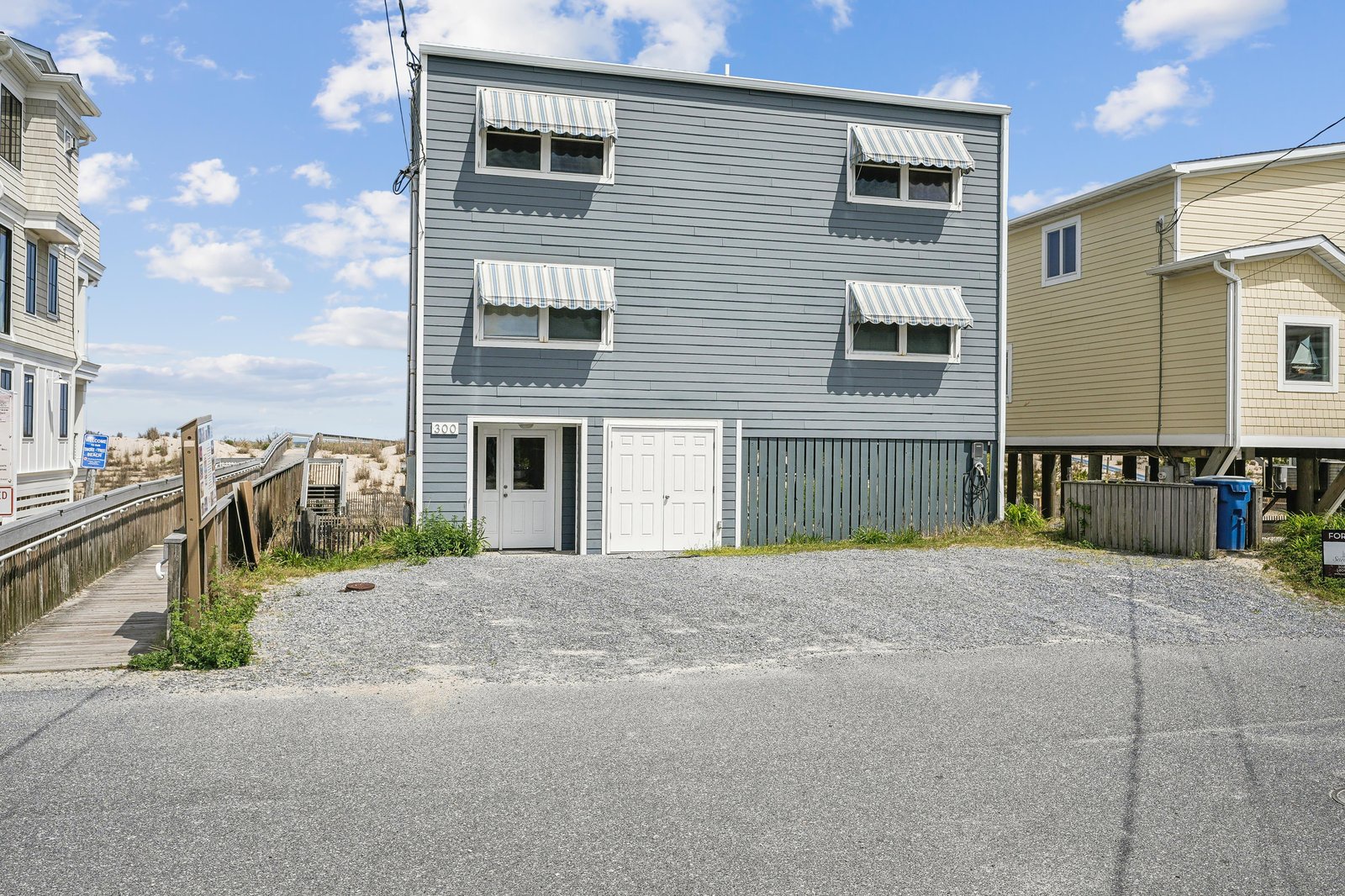 This charming blue coastal property offers convenient parking and a welcoming entrance, situated in a quiet beachside neighborhood with boardwalk access steps away.