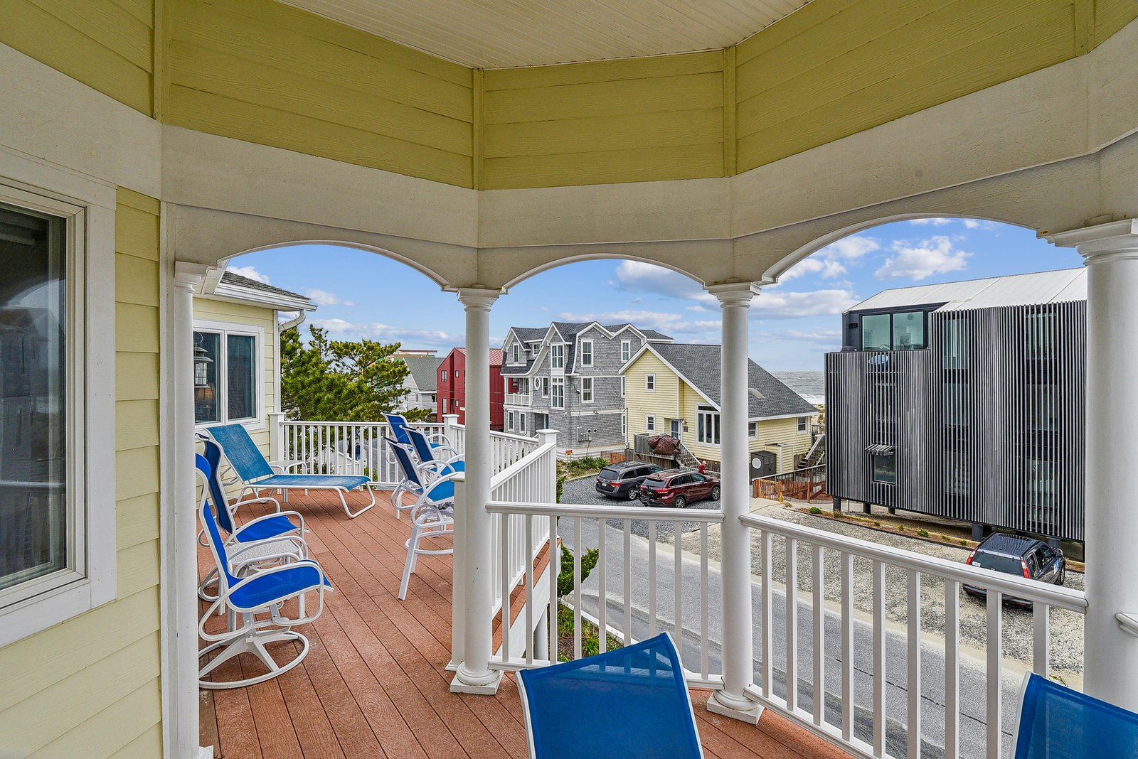 This upper-level balcony overlooks neighboring beach homes and residential streets, featuring a covered deck with classic columns and comfortable seating—an ideal spot to relax after a day of coastal exploring.