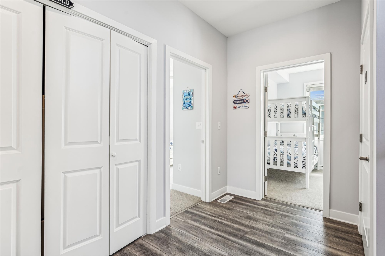 A welcoming hallway with modern wood-style flooring leads you to peaceful sleeping quarters, including a charming bunk room perfect for kids or groups. The airy, bright space features clean lines and coastal touches that make you feel right at home.