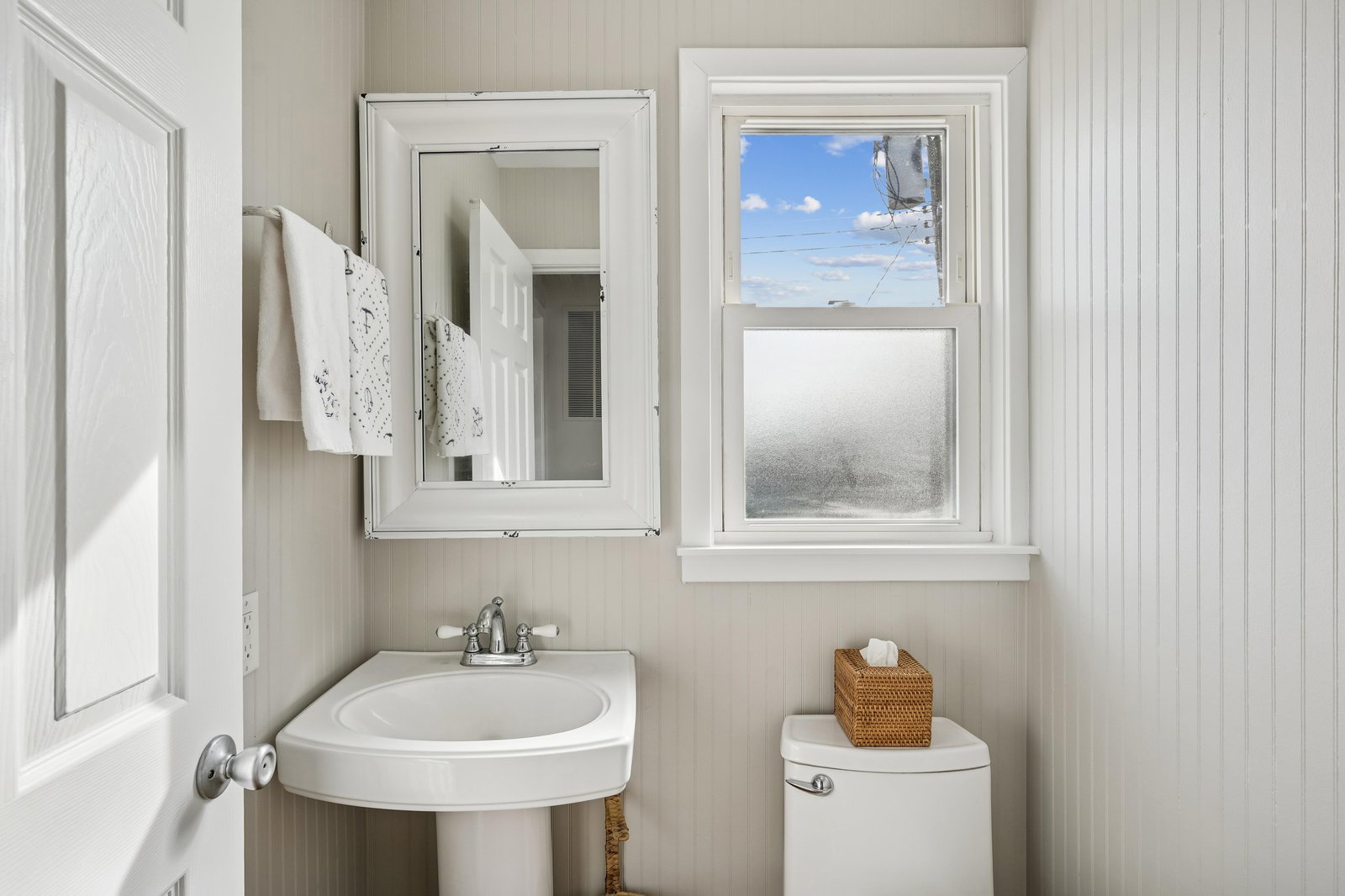 Your bright, clean bathroom features crisp white beadboard walls, a pedestal sink, and soft natural light—a refreshing space to start your day.