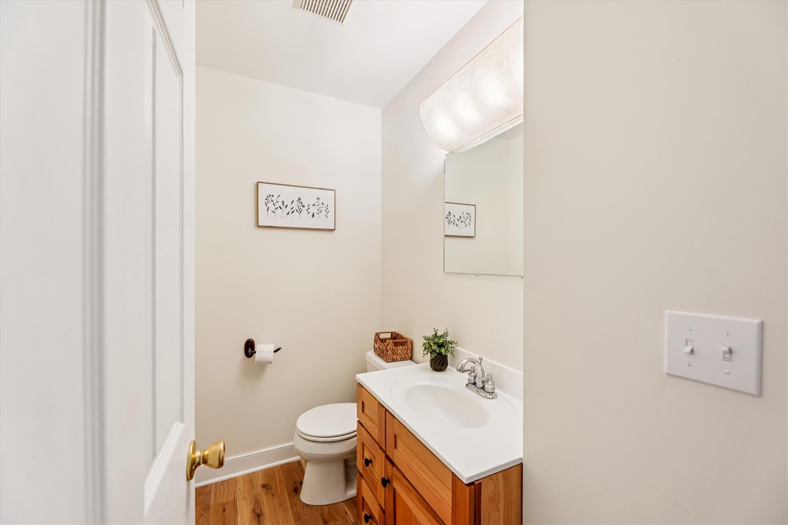 Step into your private bathroom featuring warm wood vanity, crisp white countertop, and thoughtful touches like fresh greenery and artwork.