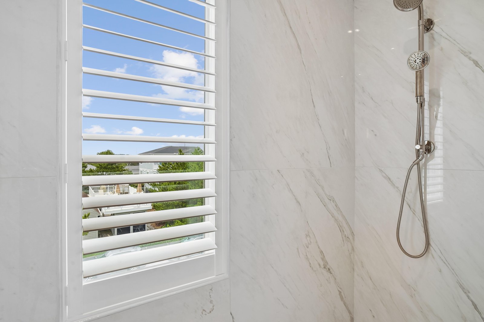 Step into your elegant marble shower with natural daylight streaming through plantation shutters. Sleek fixtures and pristine tile create a spa-like retreat for your morning routine.