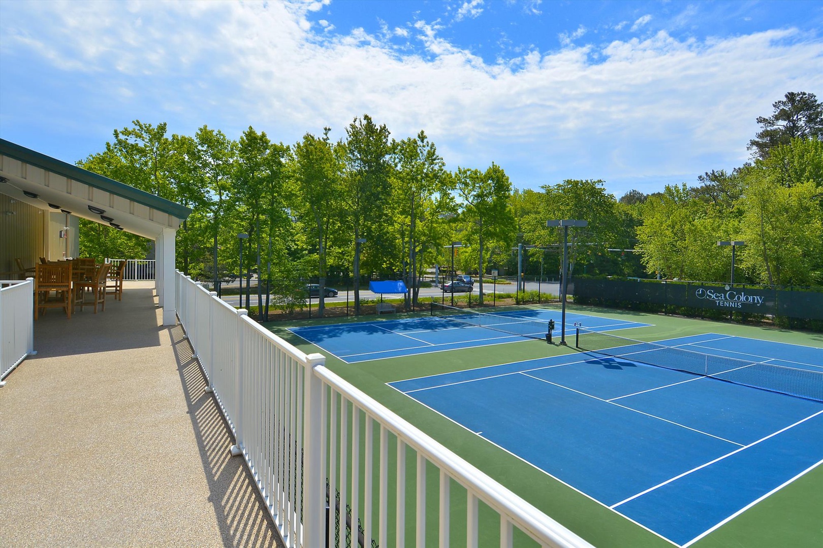 Professional tennis courts with viewing deck and seating area, surrounded by lush trees in a peaceful resort setting.