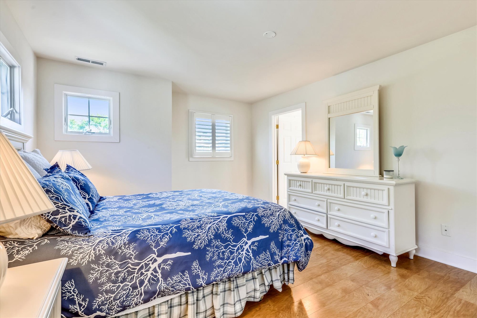 Step into your peaceful coastal retreat. Natural light pours through plantation shutters, highlighting crisp white linens and calming ocean-blue accents that promise restful nights.