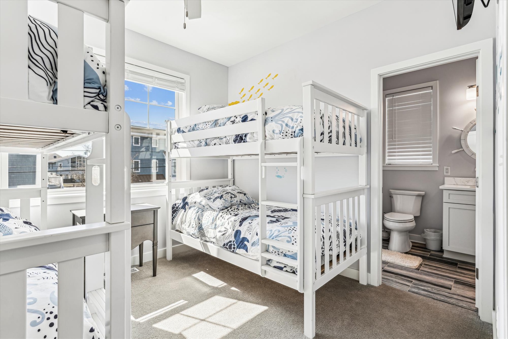 Rest peacefully in your bright bunk room with ocean-themed bedding and natural light streaming through windows.