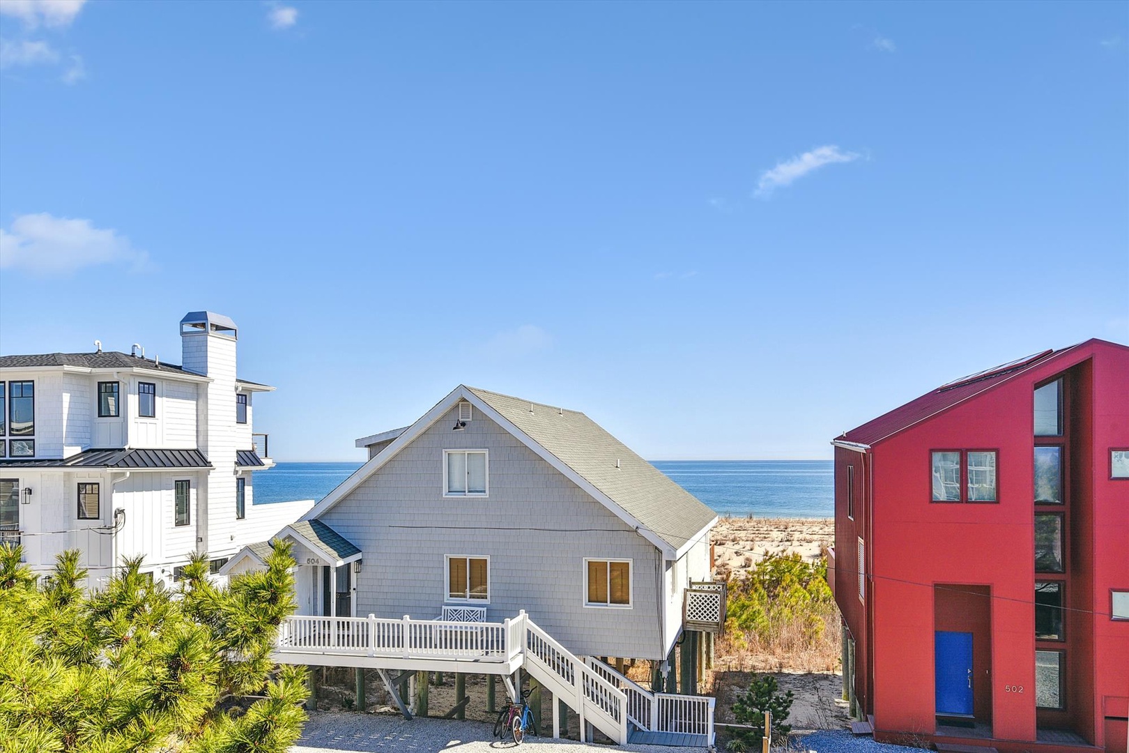 Coastal neighborhood featuring beach houses with ocean access, surrounded by natural greenery and sandy dunes under a clear blue sky.