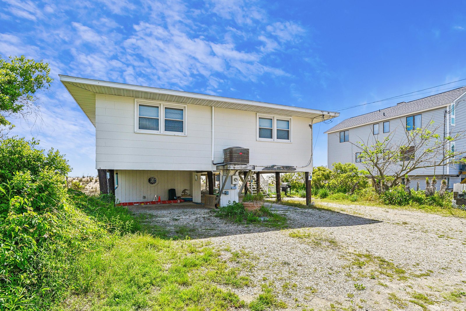 This elevated beach home features a private gravel parking area and ground-level covered patio space, set in a quiet coastal neighborhood with easy access to nearby beaches and natural surroundings.
