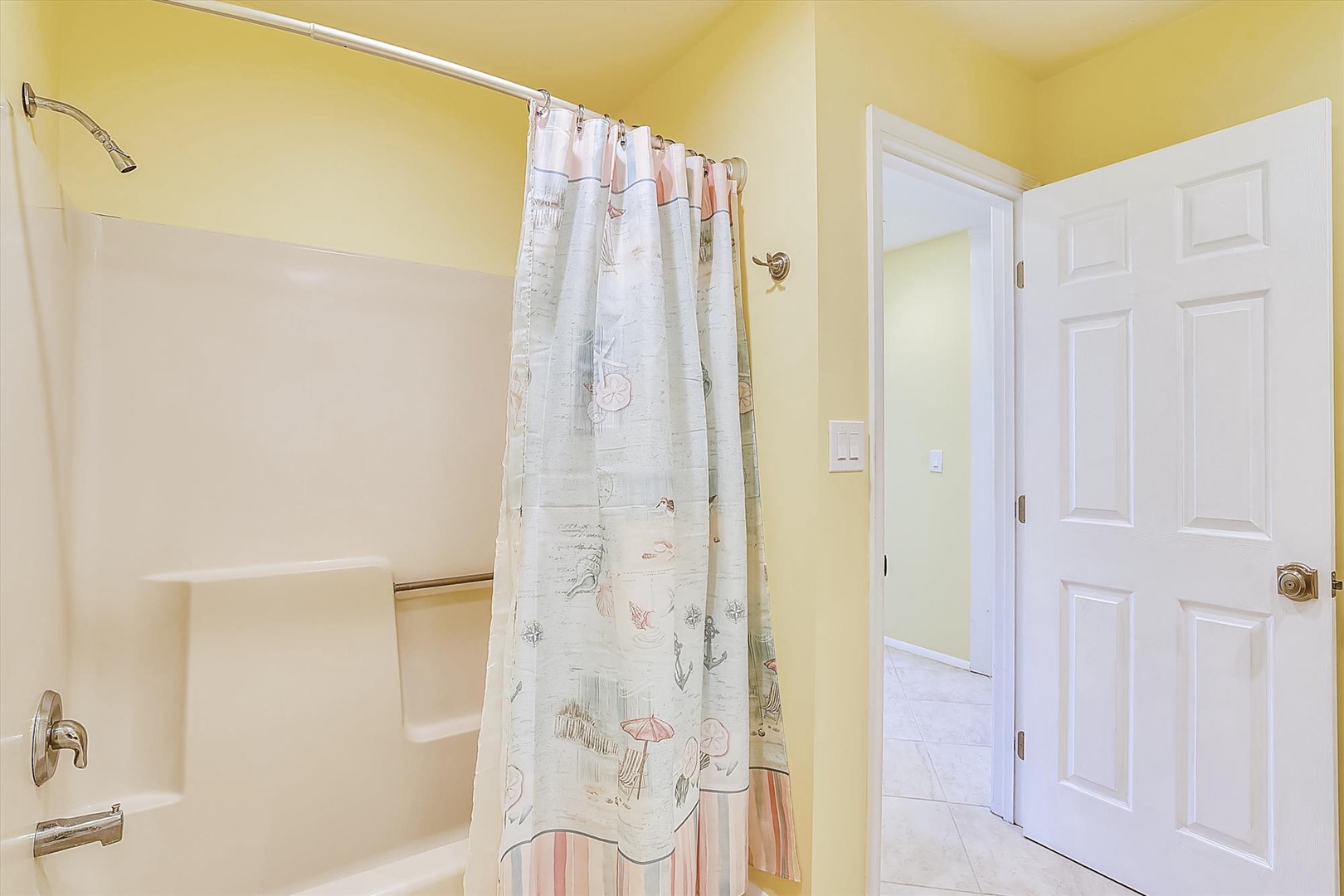 Your private bathroom features a full tub-shower combo with cheerful coastal-themed curtains, bright welcoming decor, and fresh tiles underfoot—perfect for unwinding after a day of adventure.
