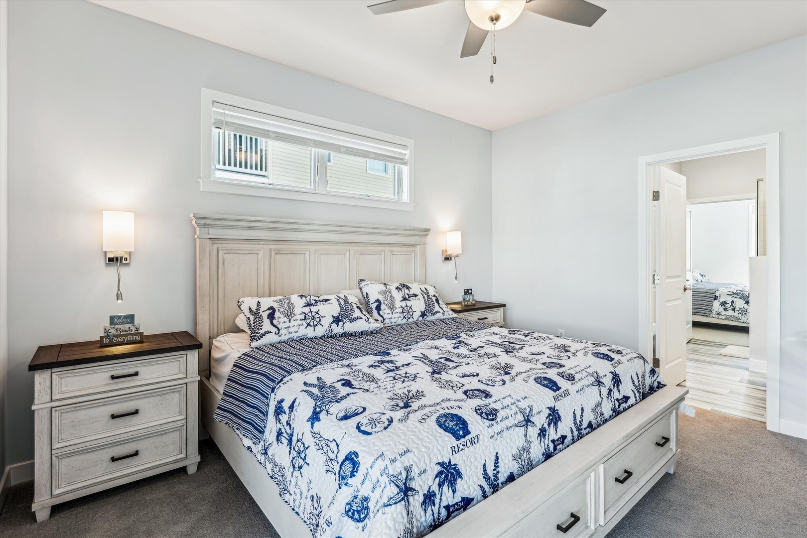 Your serene bedroom retreat features a plush king bed dressed in coastal linens, soft lighting on both sides, and a ceiling fan to keep you comfortable. The en-suite bathroom is just steps away for your convenience.