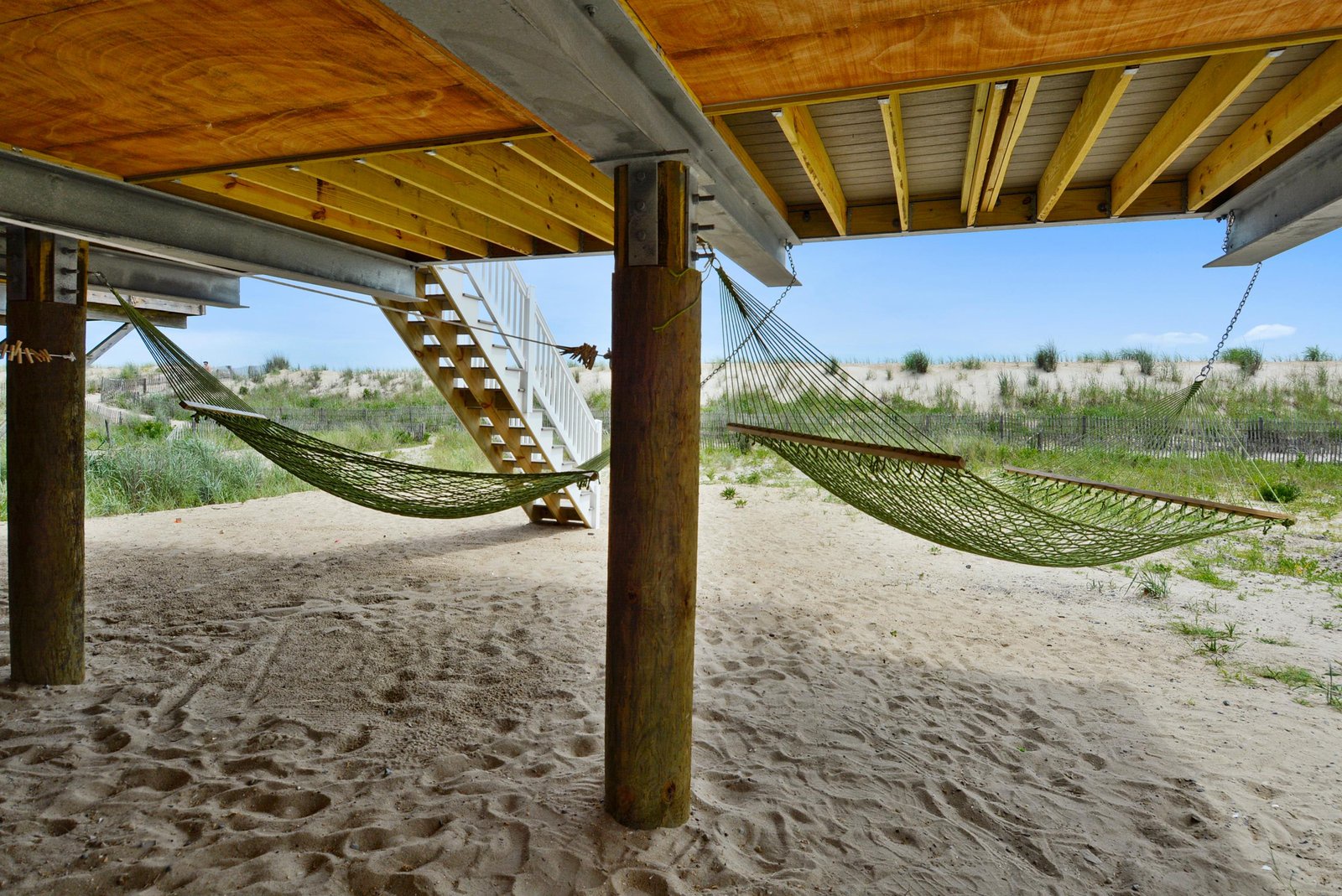A covered sandy relaxation area provides shelter and a peaceful spot to unwind just steps from the beach, with natural dunes and coastal grasses framing the horizon beyond.