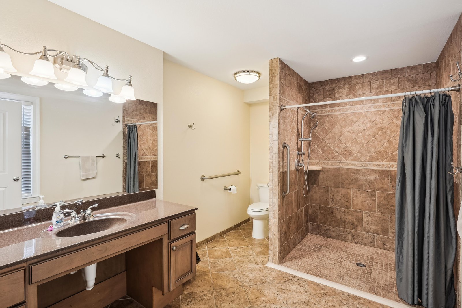 Step into your spacious, accessible bathroom with a roll-in shower, grab bars, and warm tile finishes—designed for your comfort and ease.