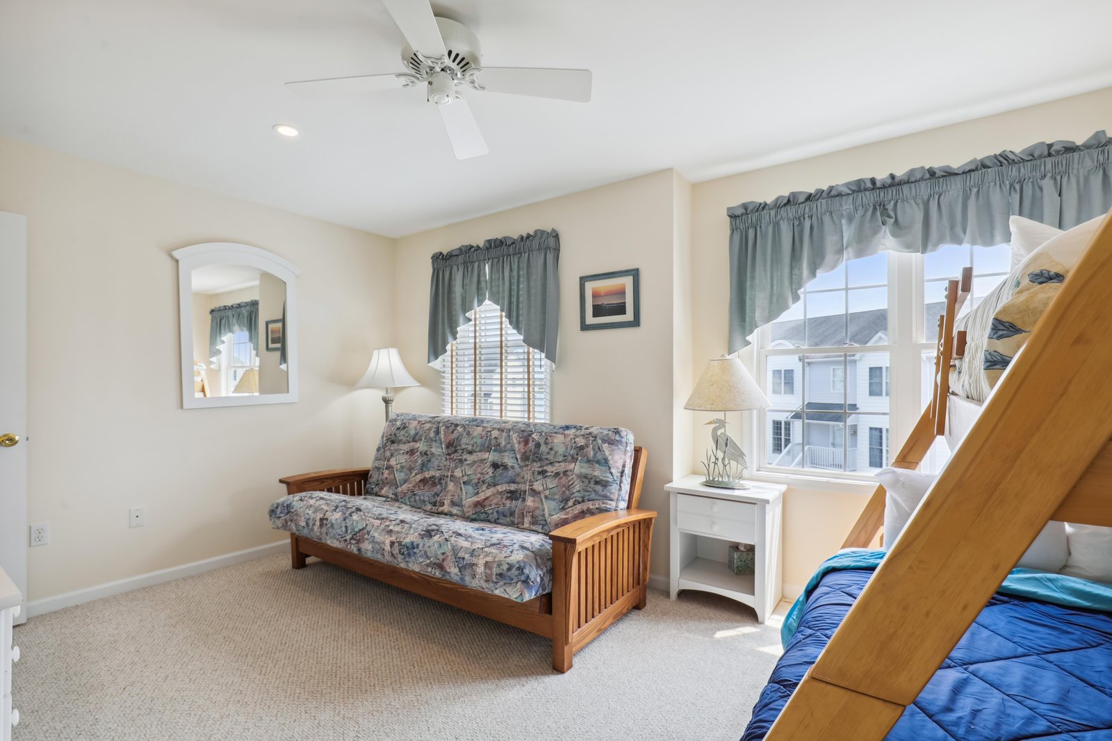 Your bright corner retreat features a plush futon, cozy bunk beds, and peaceful neighborhood views framed by soft curtains—ideal for relaxing together after a day of exploring.