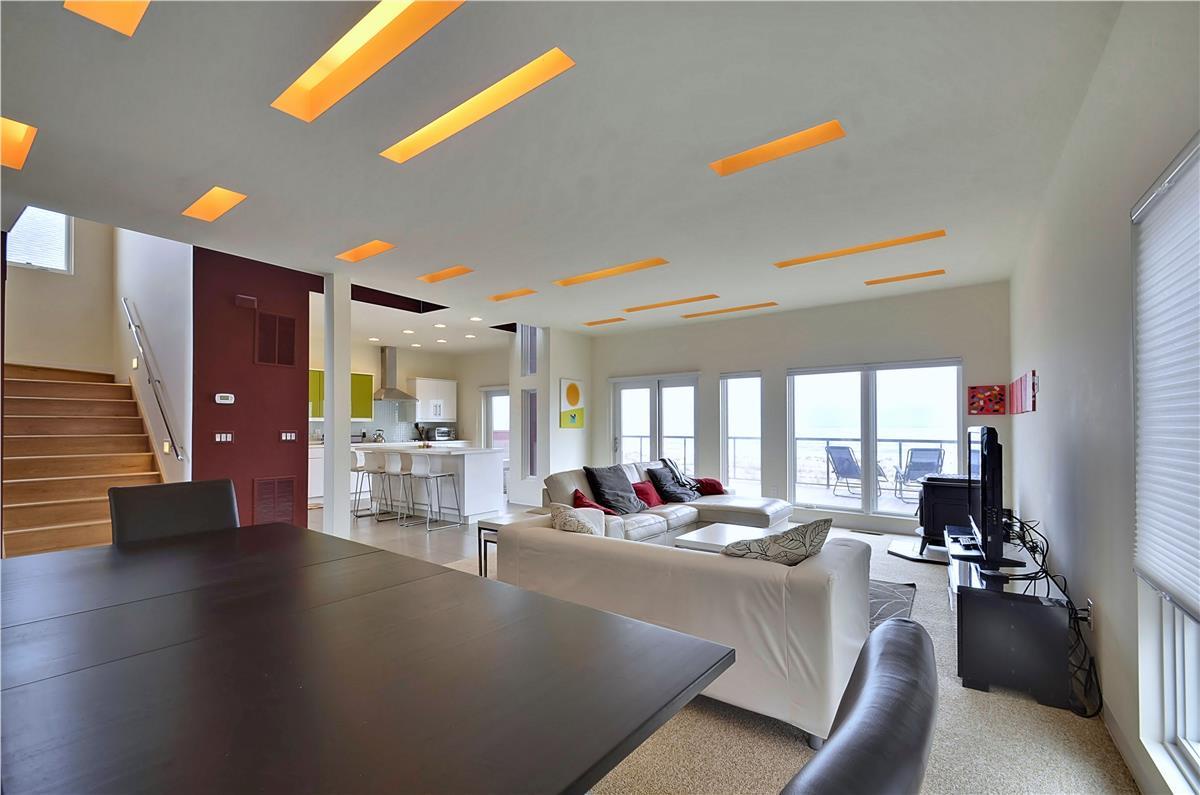 Step into a light-filled open space where bold orange ceiling accents add modern flair. Relax on plush seating or whip up a meal in your fully equipped kitchen overlooking the living area and outdoor terrace.