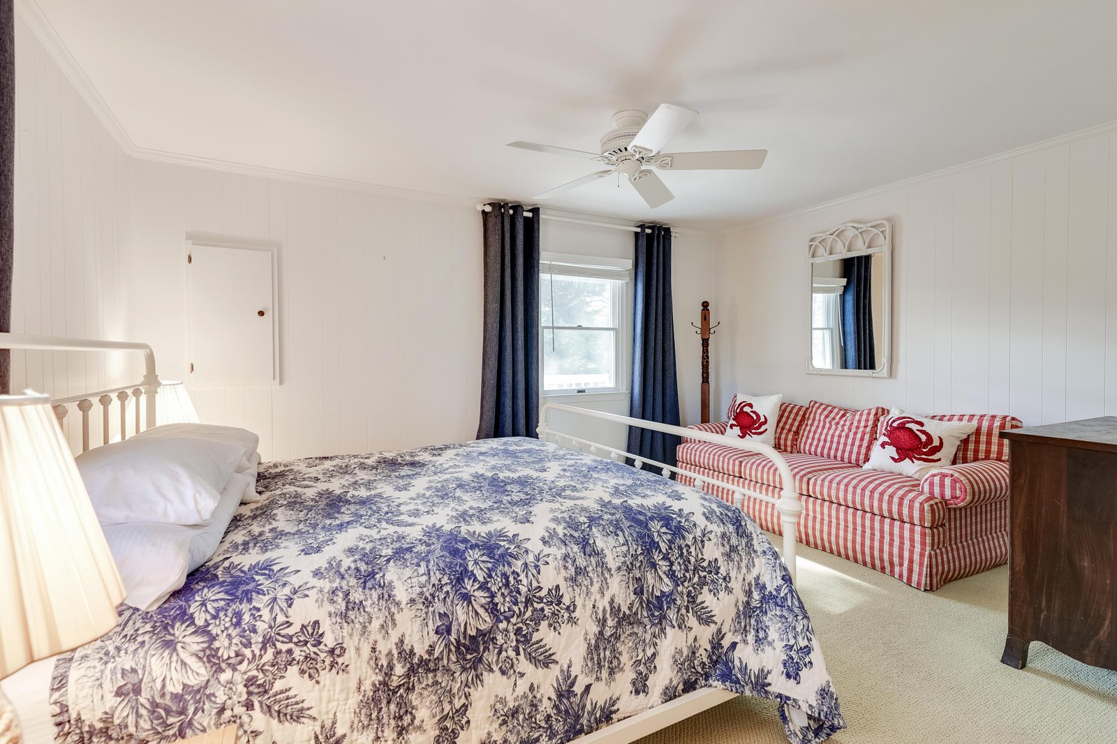 Settle into your coastal-inspired bedroom with a plush queen bed, cozy seating area, and gentle ceiling fan overhead—perfect for peaceful nights by the shore.