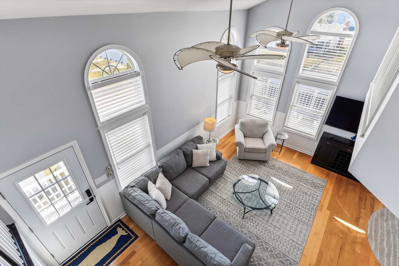 Step into your bright, airy living room where soaring ceilings and elegant arched windows flood the space with natural light. Sink into the plush sectional, unwind in your cozy armchair, and let the warm hardwood floors welcome you home.