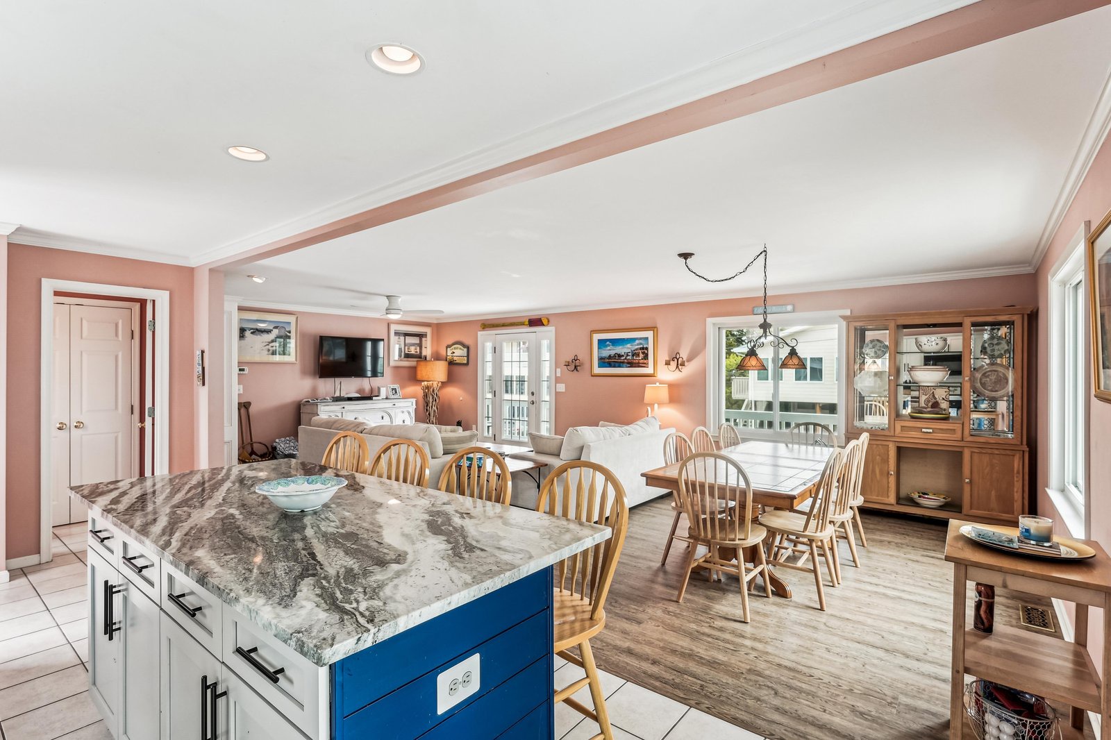 Spacious island and dining area with warm coral walls and gleaming granite. Large windows flood the open-concept space with natural light, connecting kitchen, dining, and living areas seamlessly.