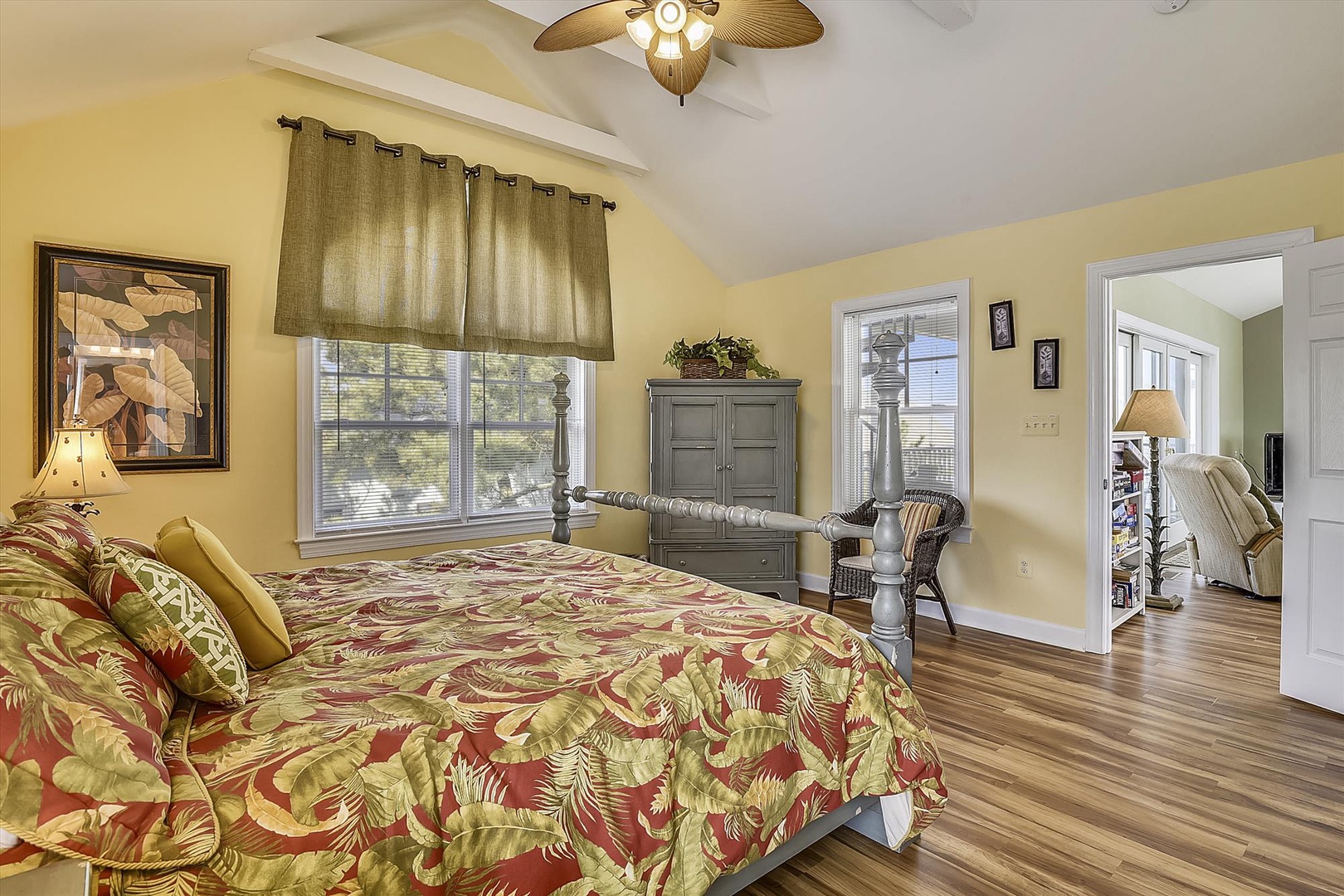 Relax in your tropical-themed bedroom with warm yellow walls, hardwood floors, and a ceiling fan keeping you cool.