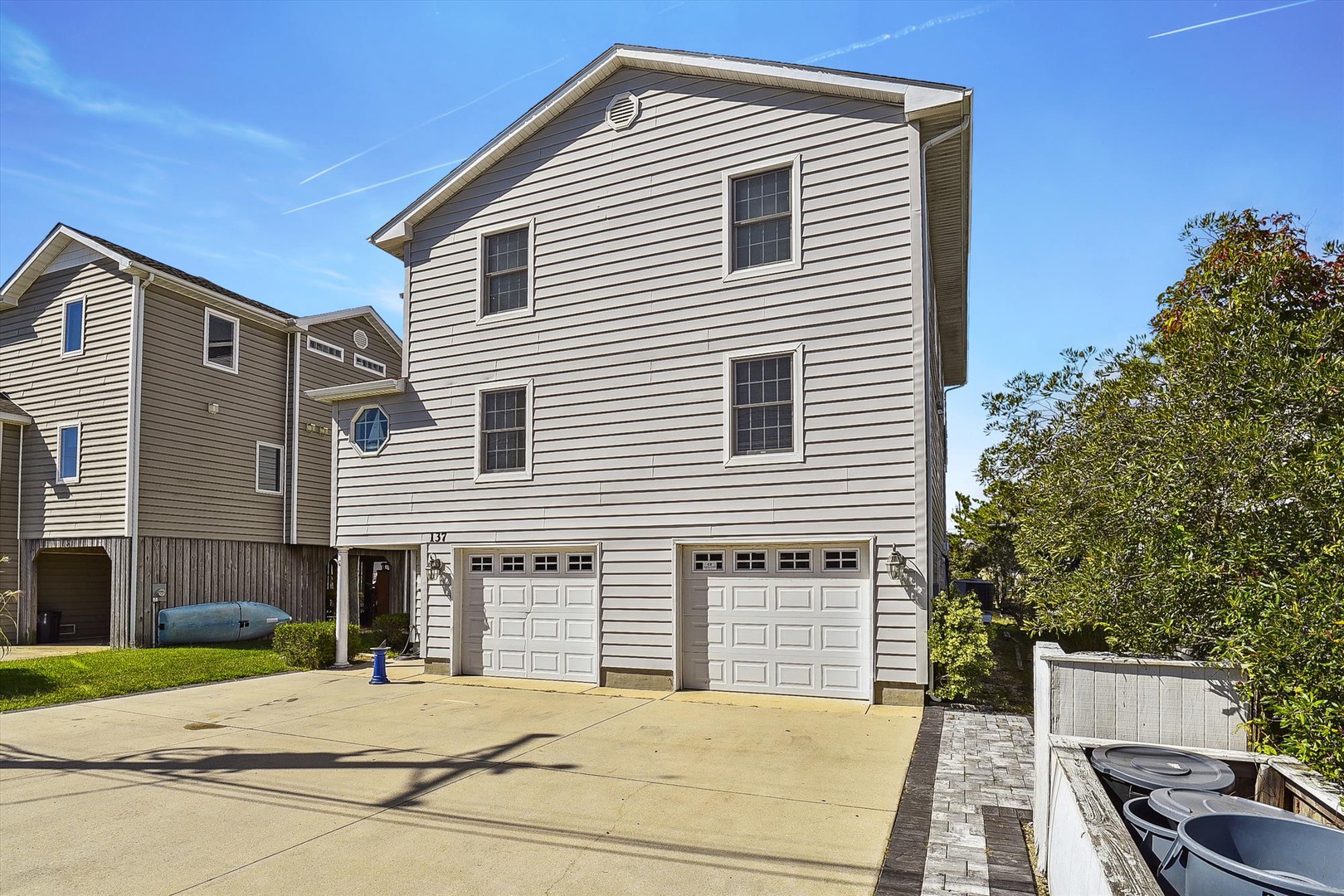 This elevated beach house features classic coastal architecture with vinyl siding and dual-car garage parking, situated in a quiet residential neighborhood near waterfront recreation.