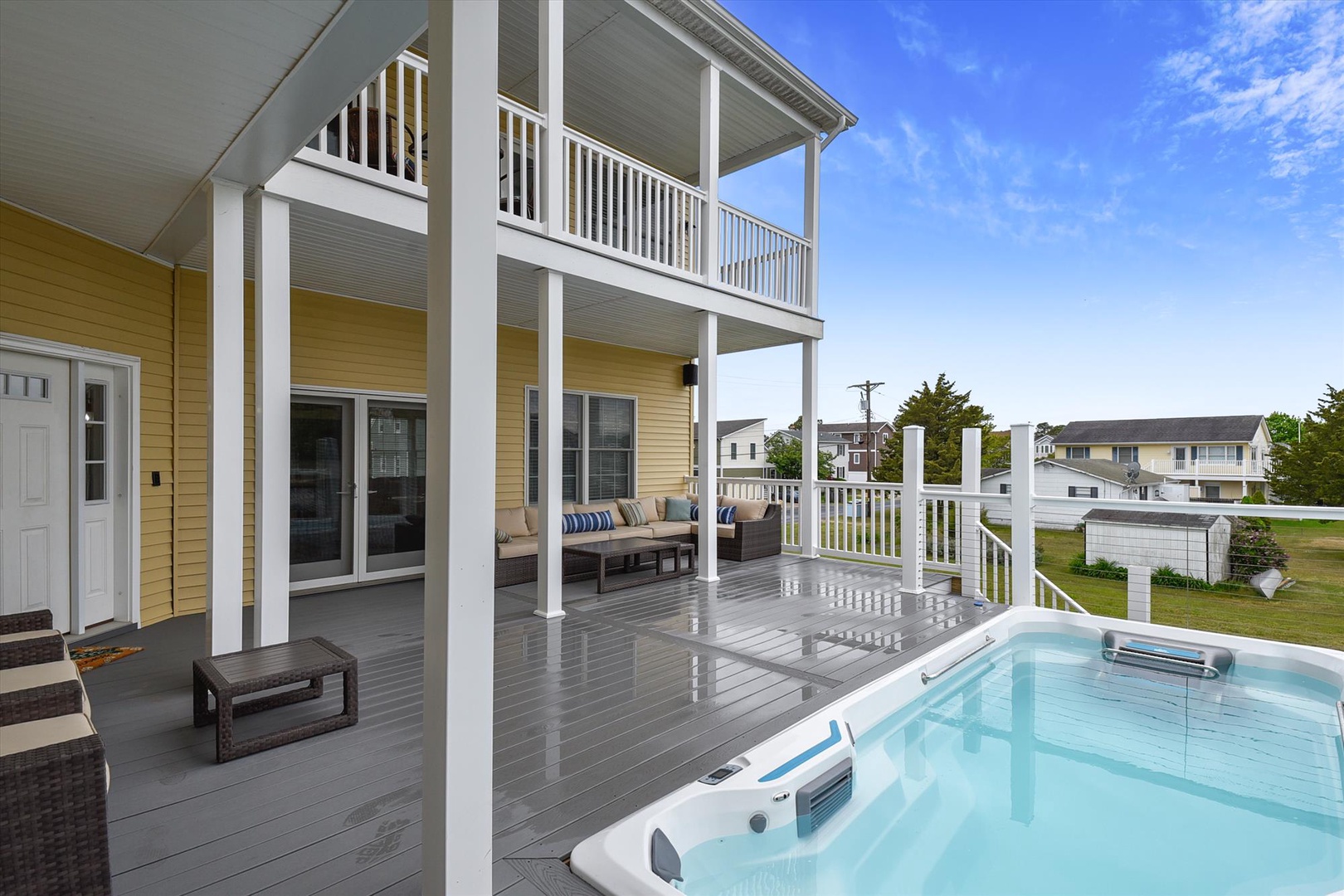 A spacious two-story deck featuring a private hot tub with comfortable lounge seating, perfect for soaking up sunshine under clear blue skies.