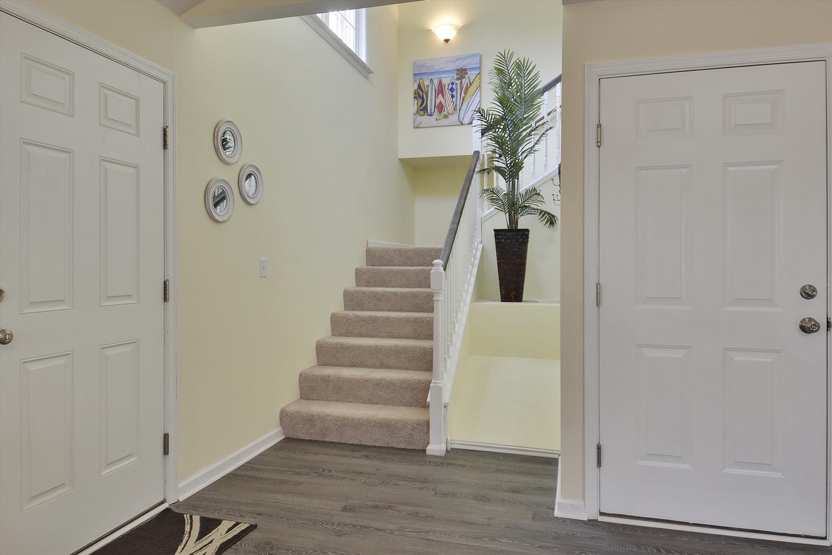 A bright, inviting entryway welcomes you with soft neutral tones, coastal artwork, and a glimpse of the staircase leading to your private retreat upstairs.