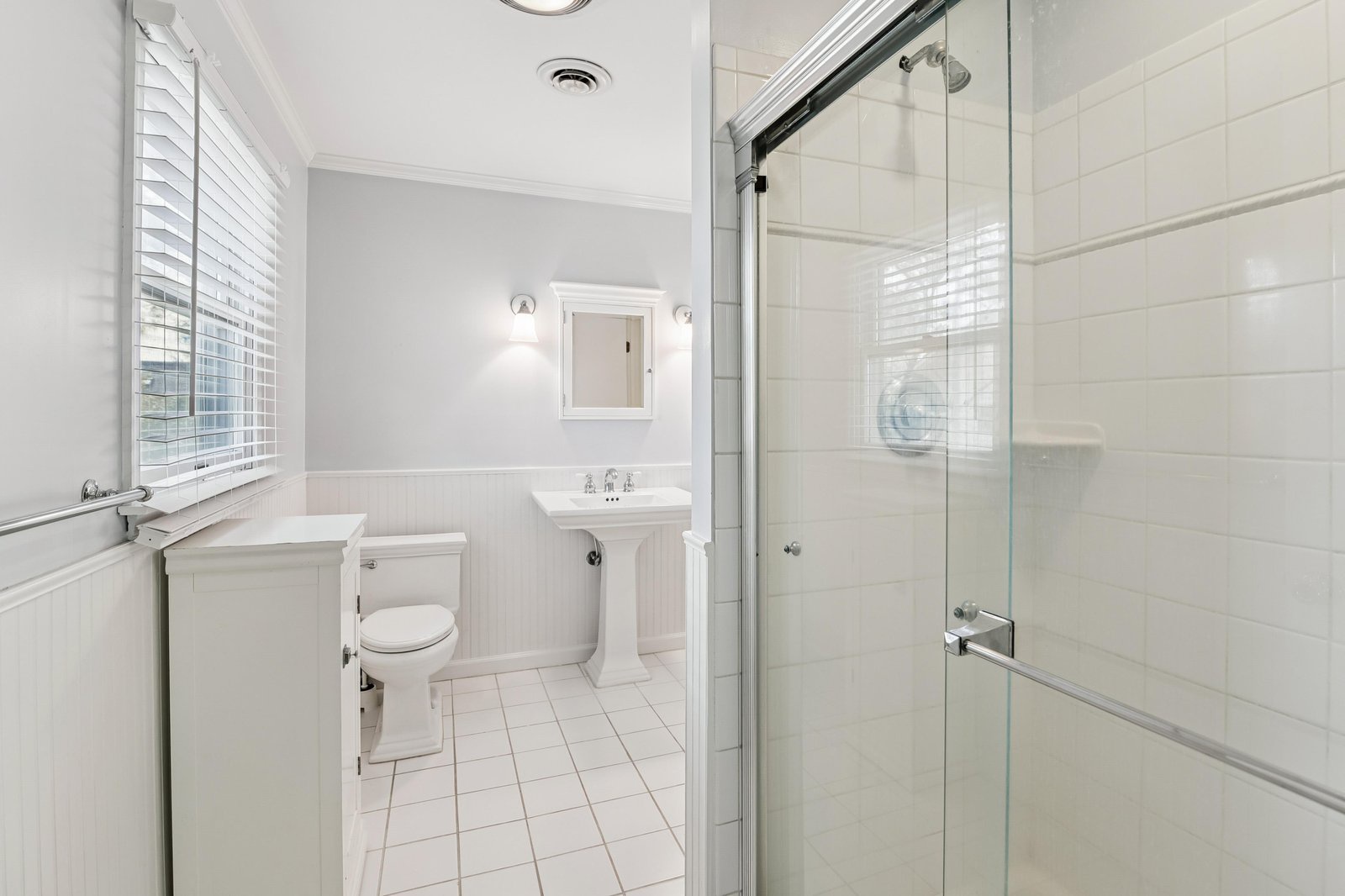 Your bright, pristine bathroom features crisp white tile, a spacious walk-in shower, and natural light from the large window—perfect for refreshing morning routines.