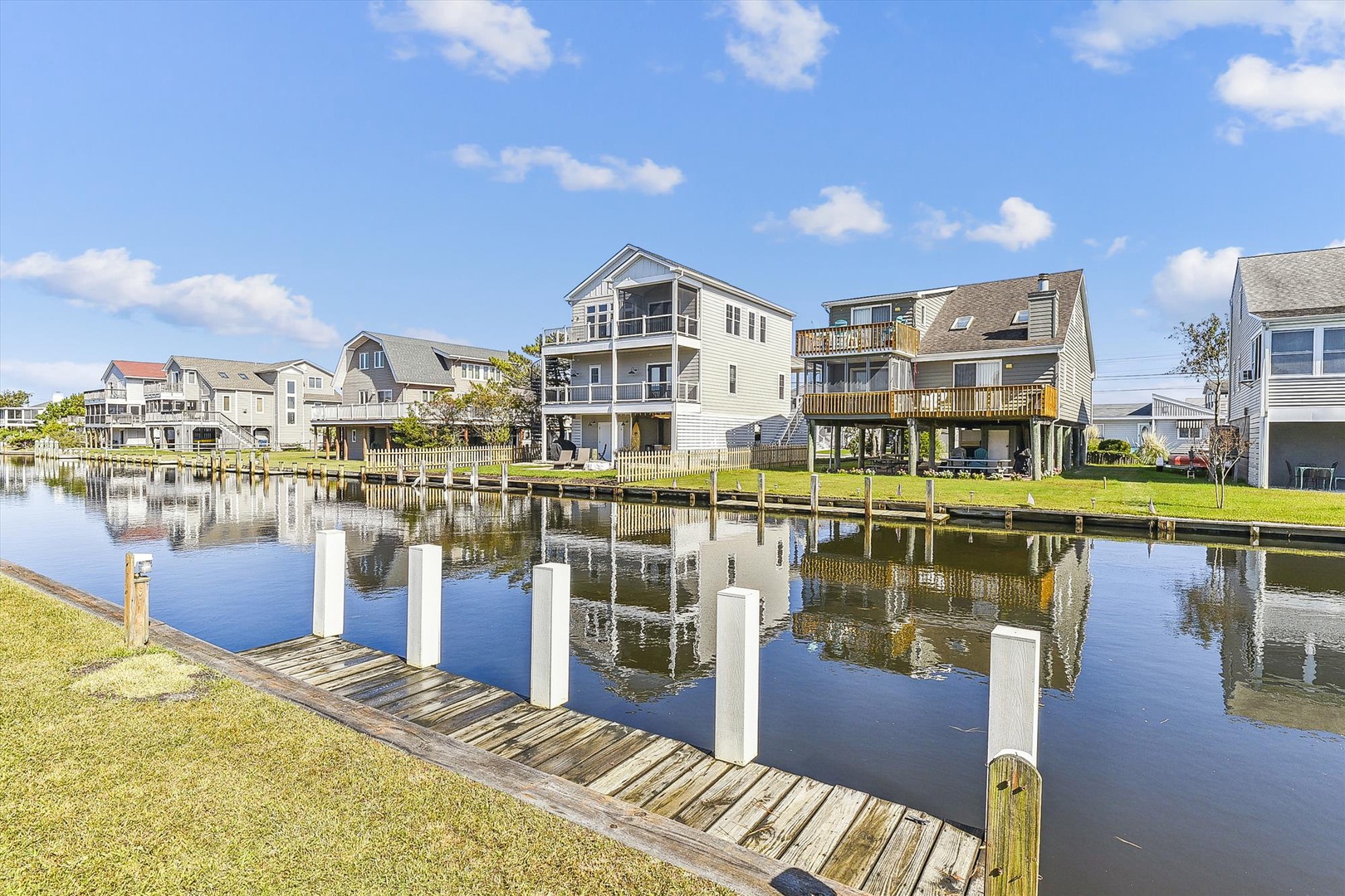 Waterfront vacation rentals line a tranquil canal with private docks, offering boating access and scenic reflections under clear blue skies.