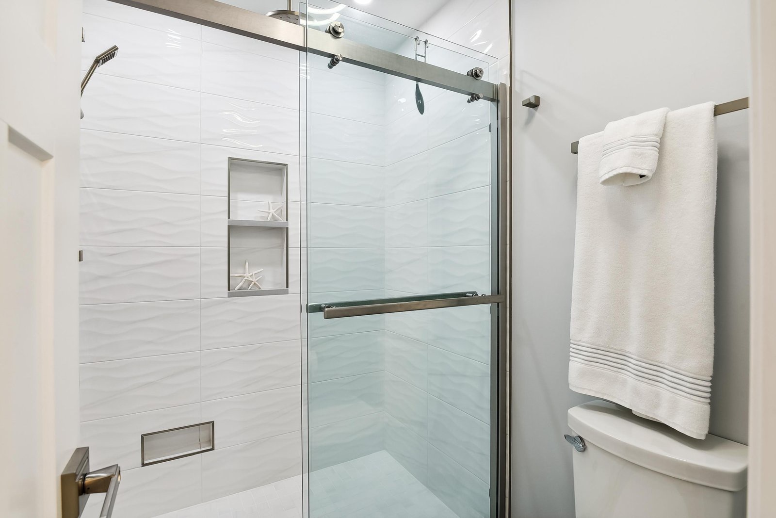 Step into your spa-inspired bathroom and unwind in a beautifully tiled walk-in shower with modern glass doors and plush white towels waiting for you.