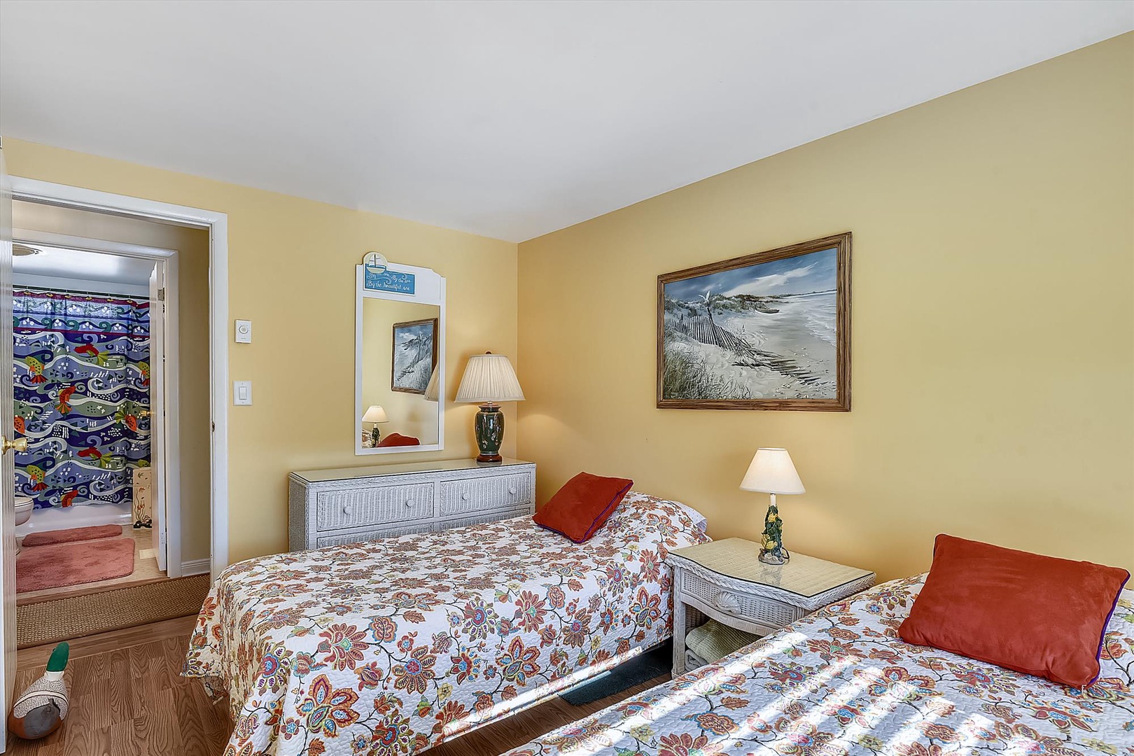 Unwind in your cheerful coastal bedroom with two cozy beds dressed in vibrant floral linens and warm coral accents that capture the beachy vibe perfectly.