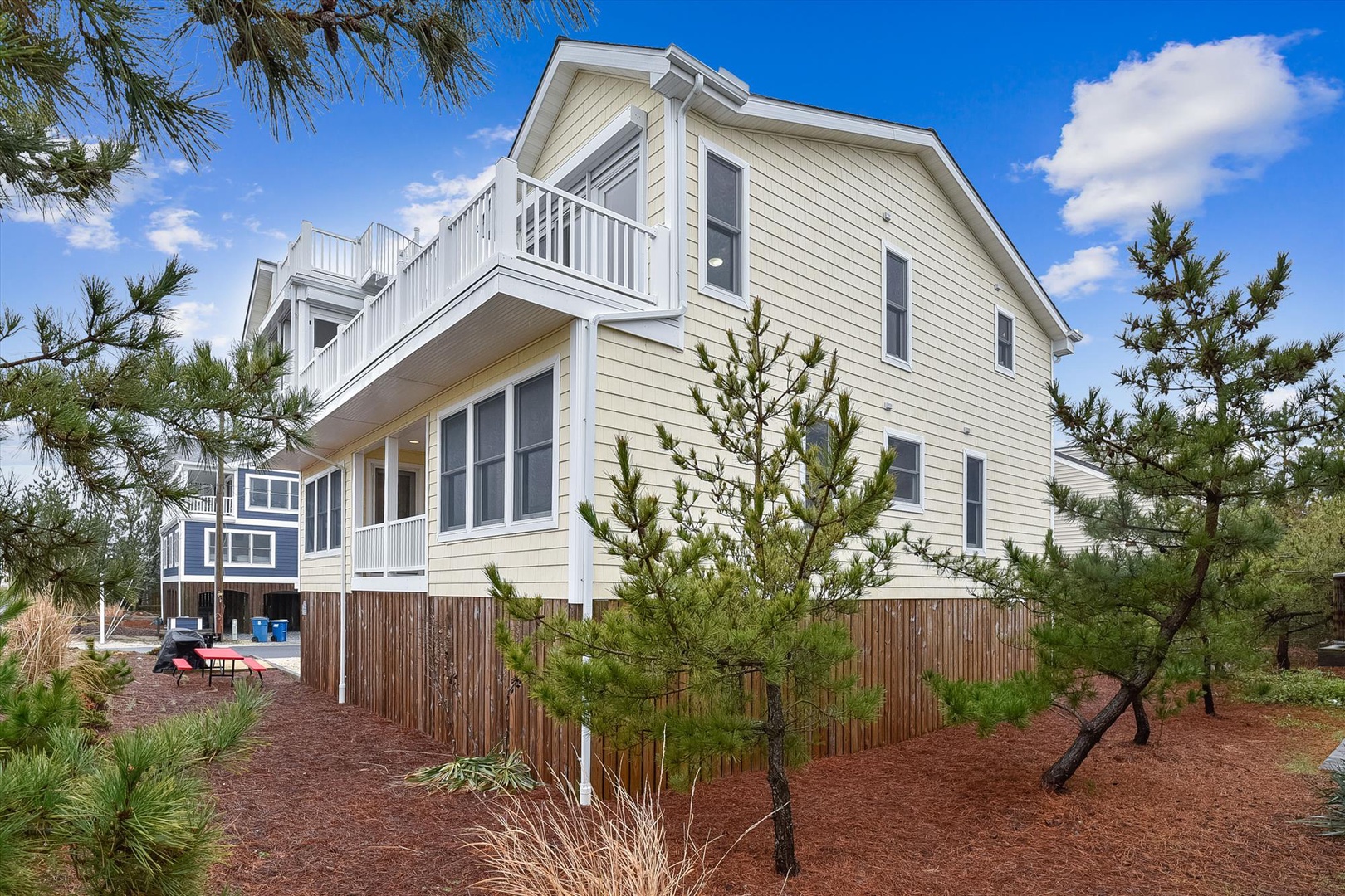 A modern coastal vacation home framed by pine trees, featuring multiple balconies and spacious outdoor areas ideal for family getaways.