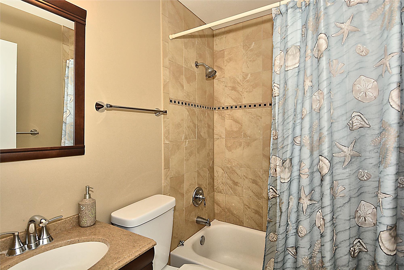 Step into your private bathroom with coastal charm—soft beige tile, a relaxing tub-shower combo, and delightful seashell accents to make you feel right at home by the shore.