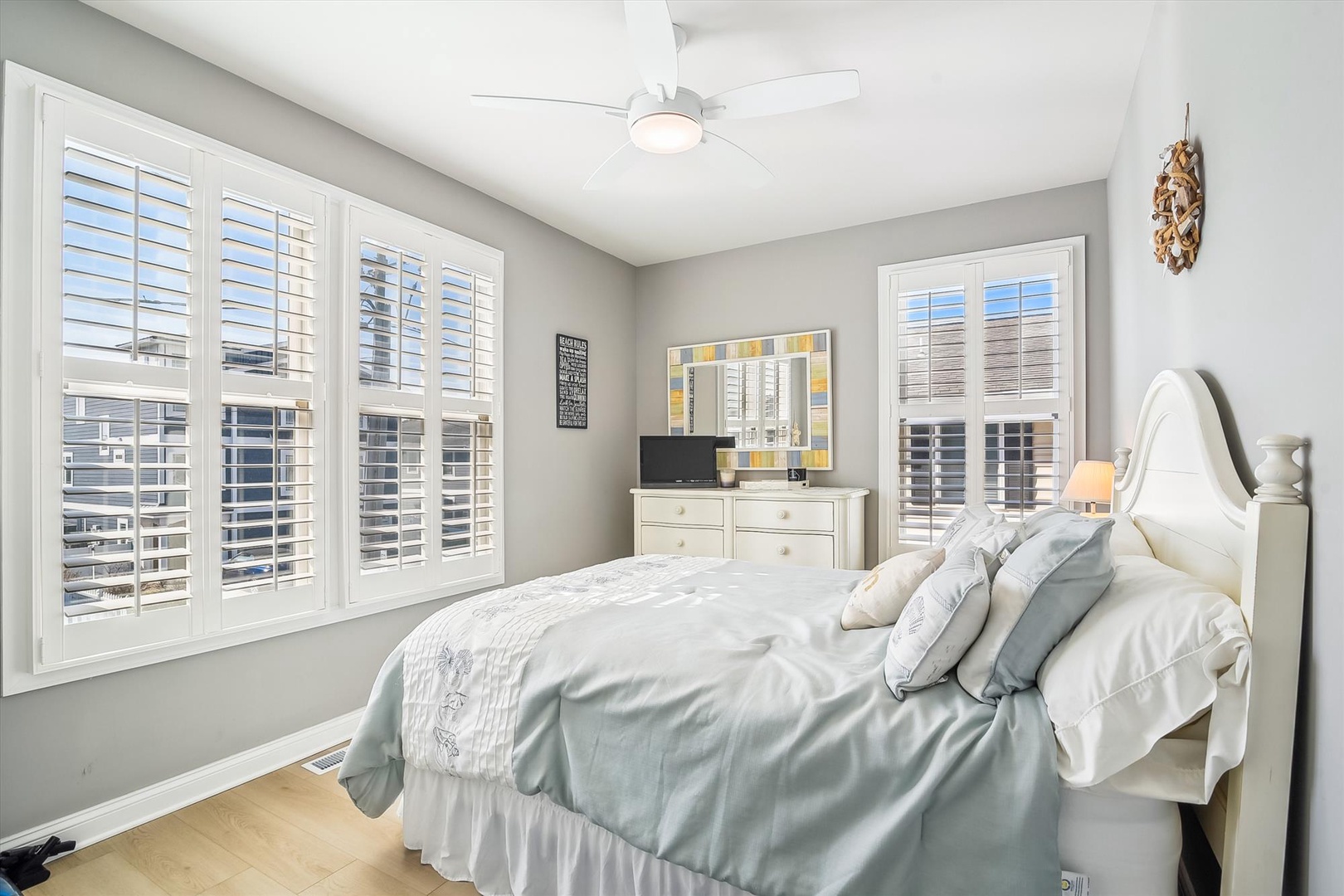 Drift off in this serene bedroom with soft coastal tones, a plush bed, and gentle breeze from the ceiling fan—your peaceful retreat awaits.