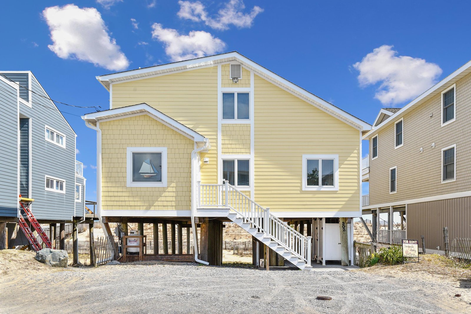 Charming coastal home elevated on pilings with bright yellow siding and crisp white trim, steps from the shore. Convenient parking and an inviting stairway welcome you to this beachside retreat.