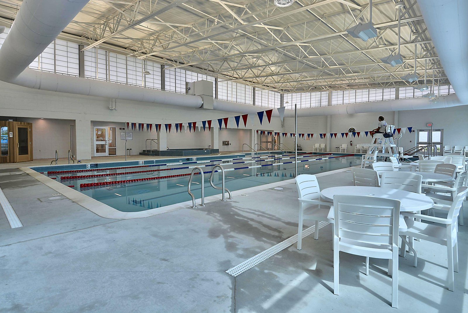 Spacious indoor lap pool features lane markers, a lifeguard station, and poolside seating under a bright, airy skylight—perfect for your morning swim or a relaxing afternoon by the water.