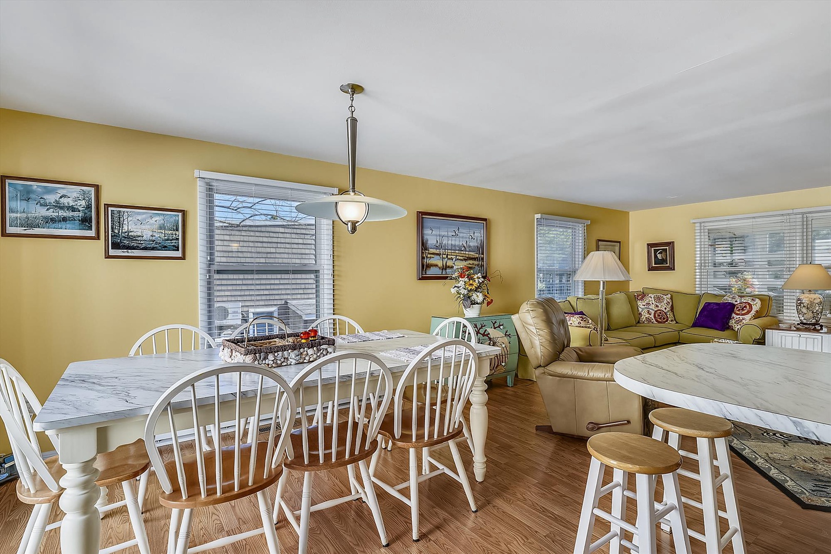 Gather around the bright, open dining and living space where sunny yellow walls and coastal artwork create a cheerful seaside retreat perfect for family meals and relaxation.