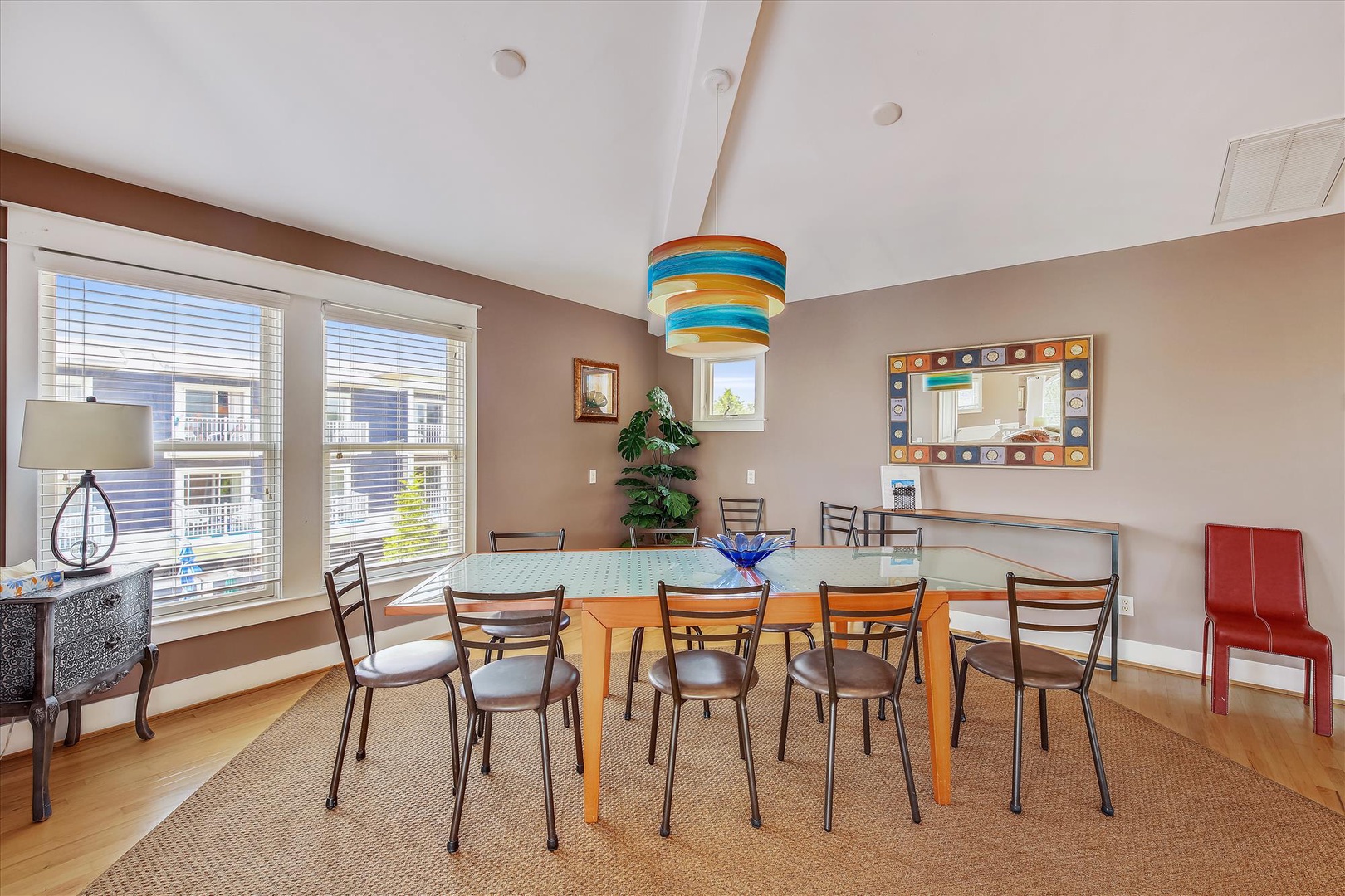 Gather around this spacious dining table for meals and conversations, where natural light pours through large windows and a vibrant pendant lamp adds a cheerful pop of color overhead.