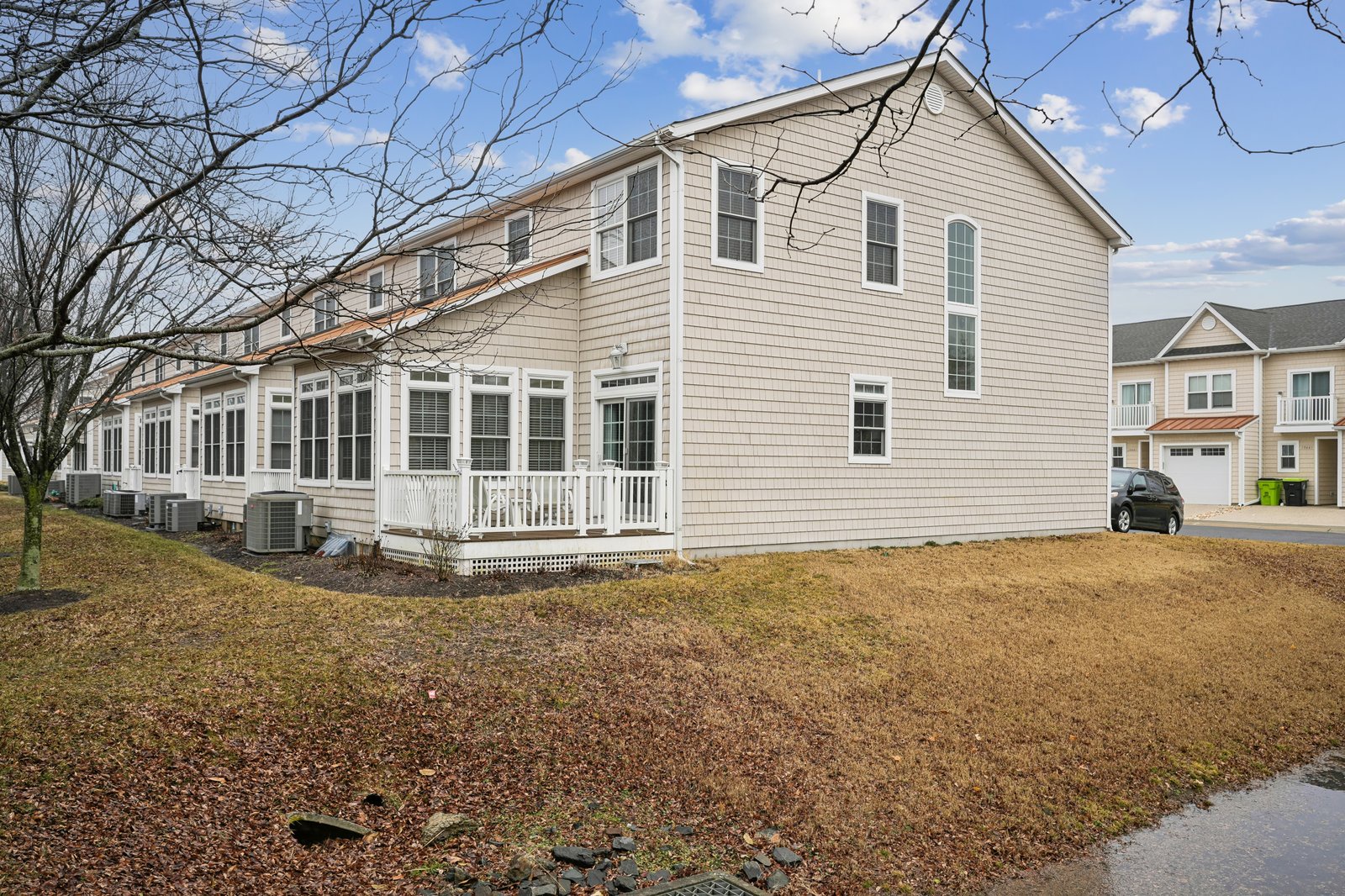 Charming beige shingled house with white trim sits in quiet residential neighborhood with mature trees and spacious yard.