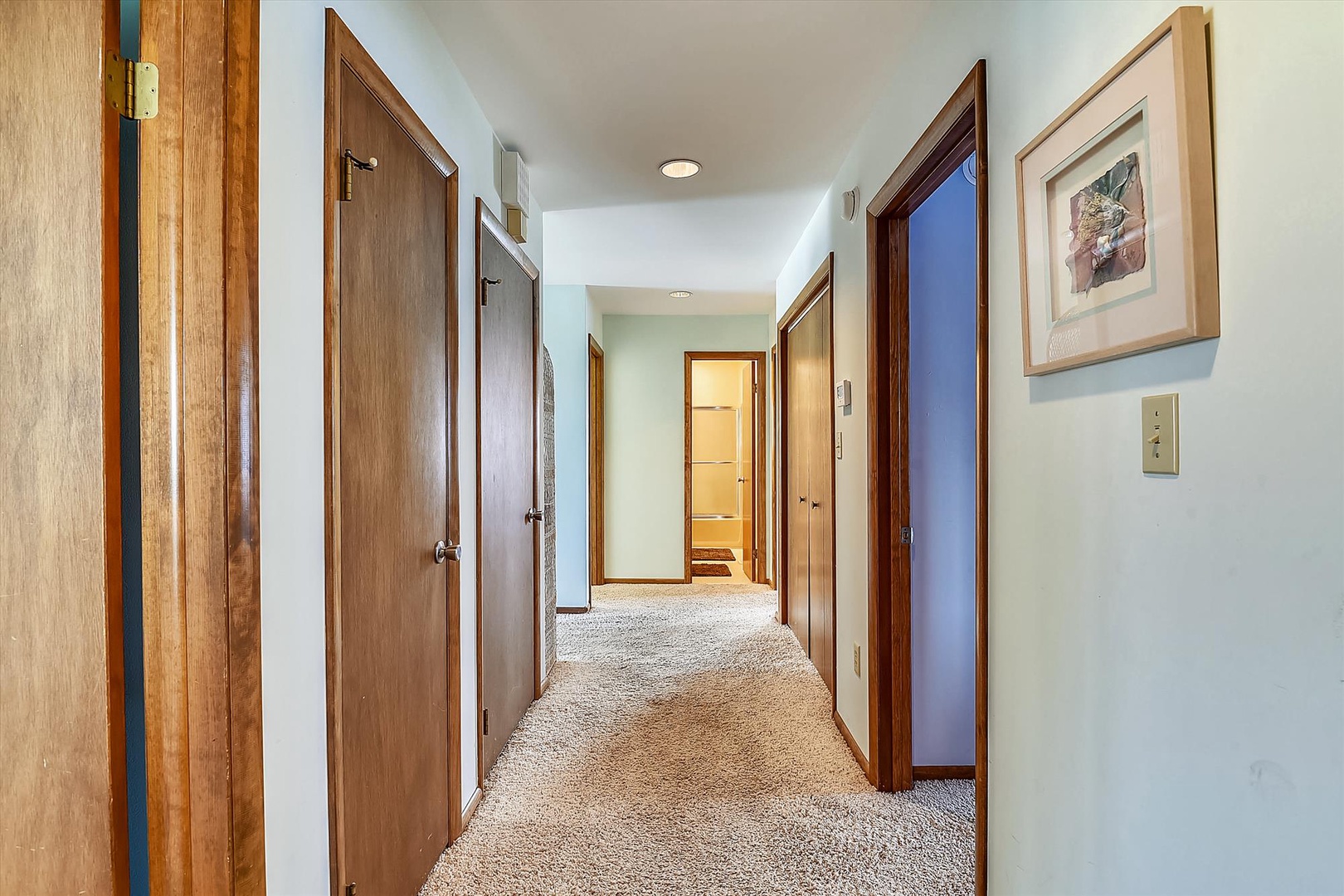 Step into your peaceful private hallway, where warm wood doors and soft carpeting lead you to each thoughtfully arranged room, making the space feel truly like home.