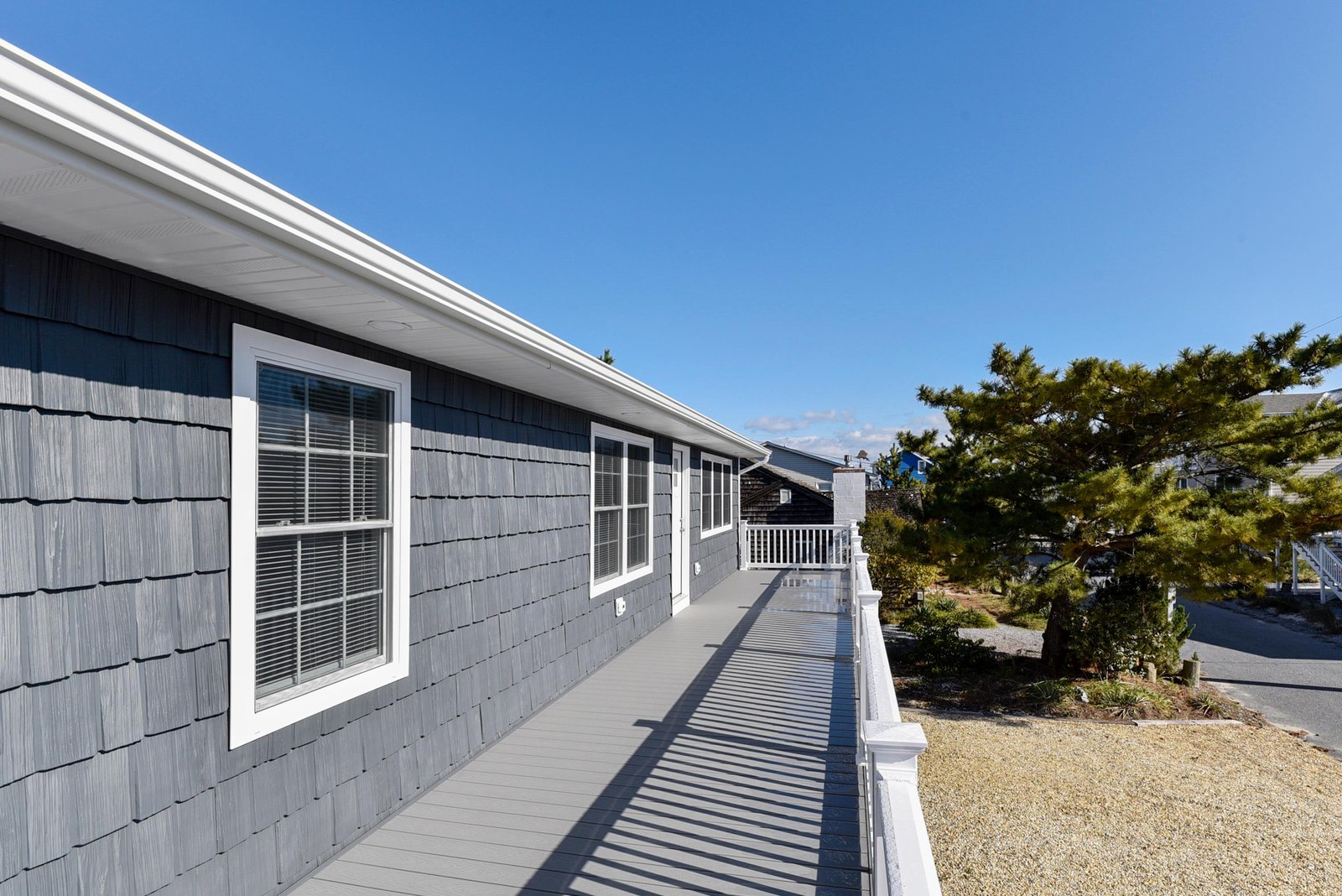 The property features classic coastal architecture with charming gray shingle siding and a white-railed deck, set in a peaceful neighborhood just steps from the shore.