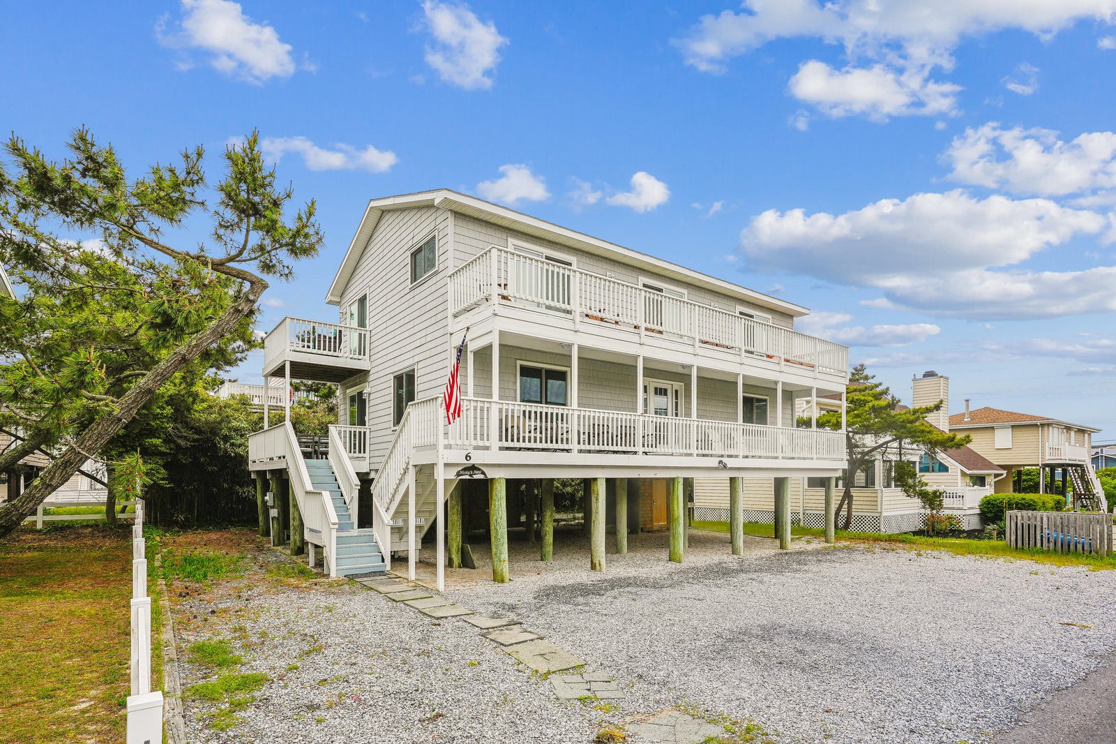 Coastal-style raised beach house featuring wraparound balconies, plenty of parking, and a welcoming entrance. The elevated design offers protection while maintaining classic coastal charm in a quiet neighborhood setting.