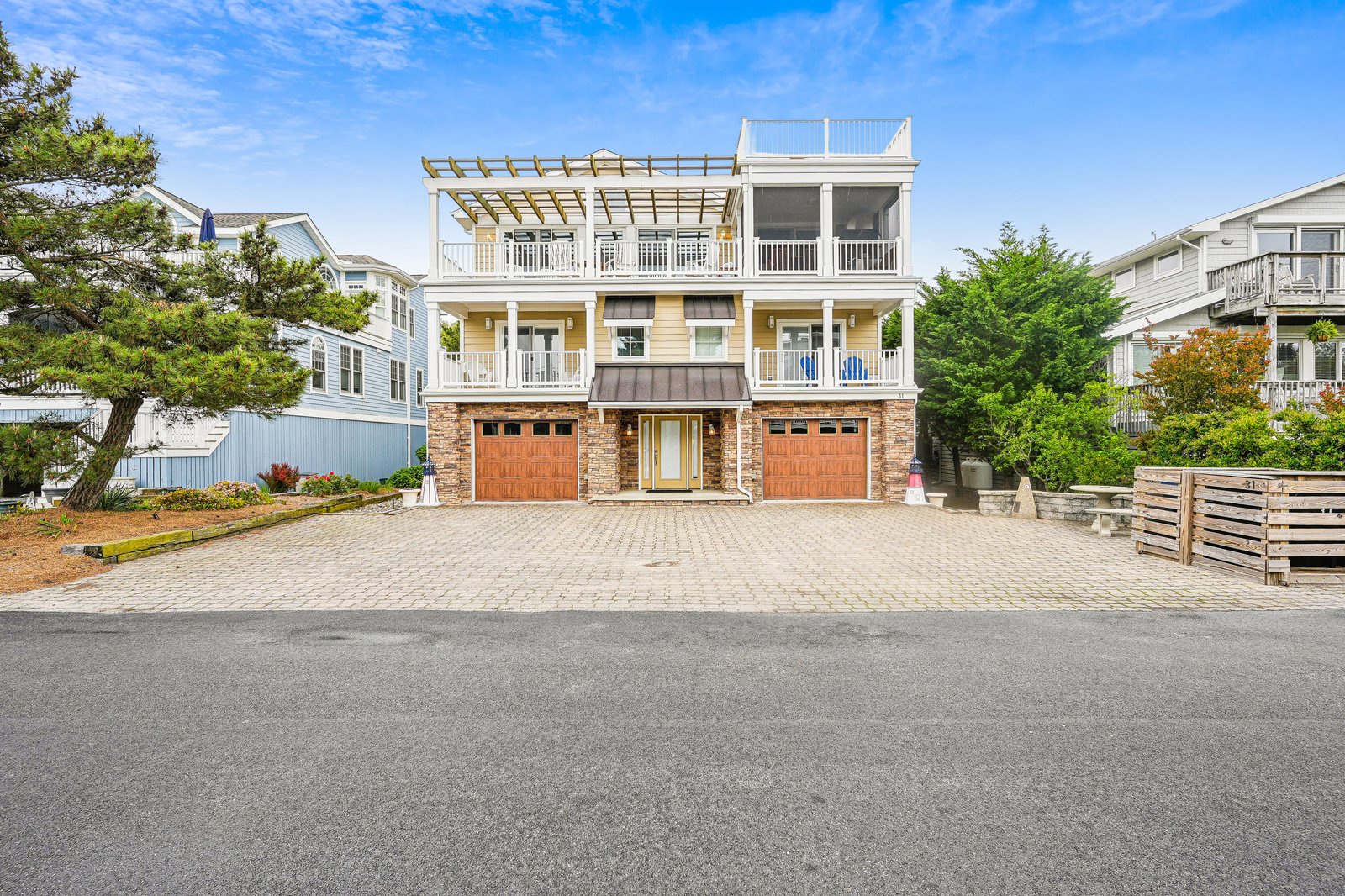 A spacious beach house with multiple decks and rooftop terrace situated in a quiet residential neighborhood, featuring ample parking and coastal landscaping.