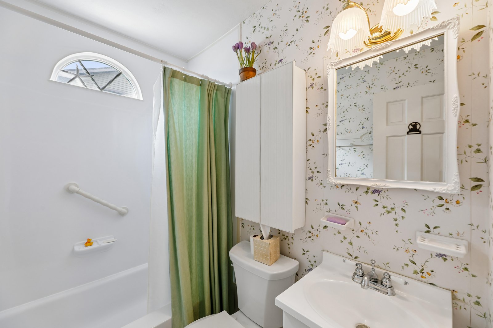 Freshen up in your charming cottage-style bathroom, where soft floral wallpaper, warm lighting, and a soaking tub invite relaxation after a day exploring the area.