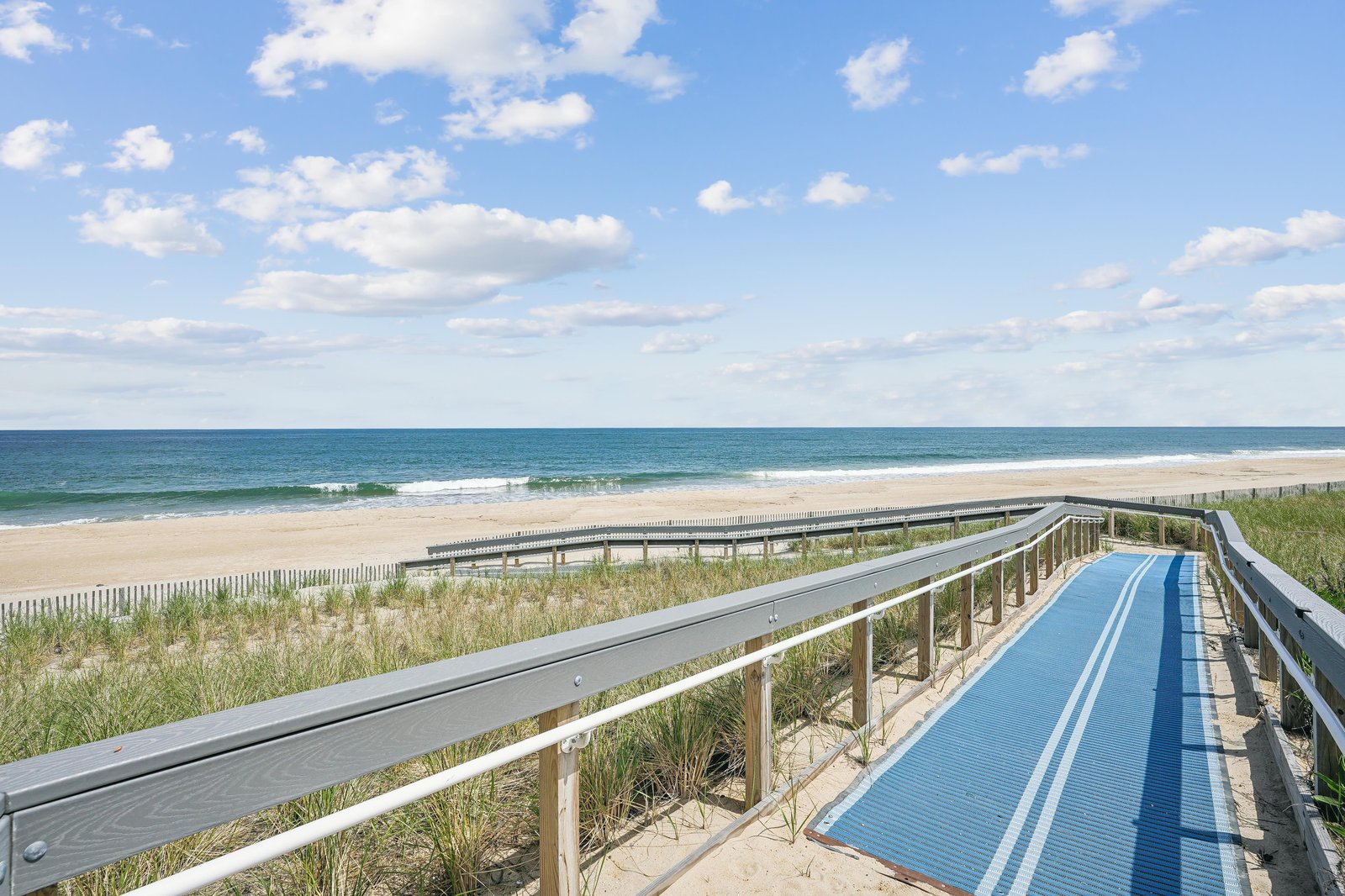 This accessible boardwalk leads directly to pristine sands and sparkling turquoise waters, framed by gentle dunes and clear coastal skies.