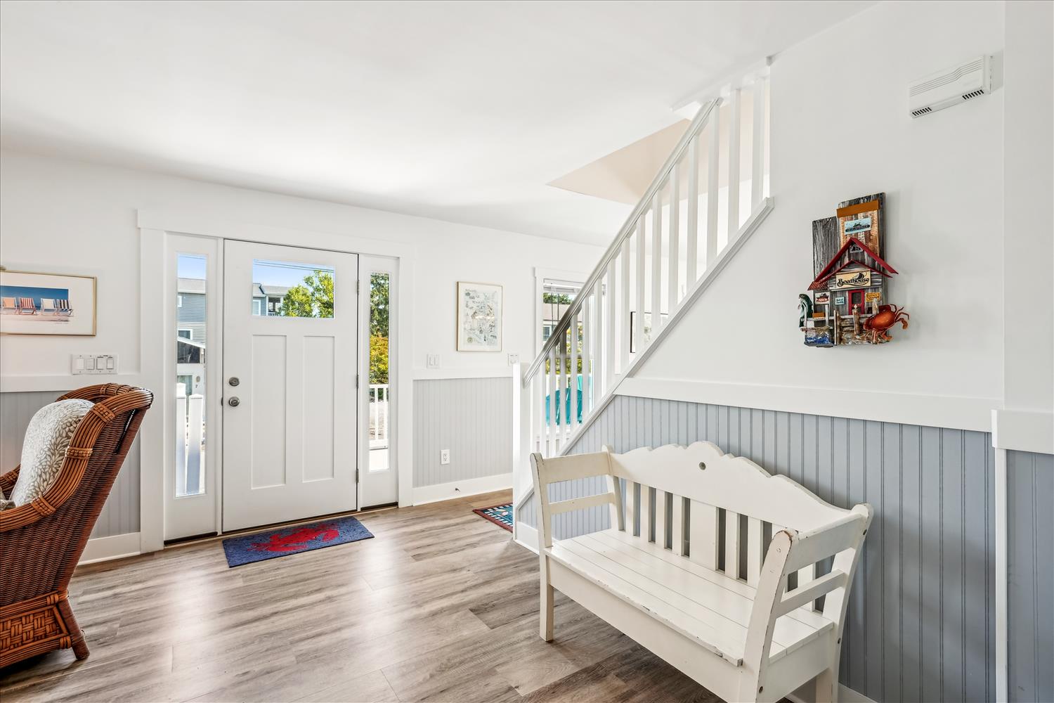 Step into your bright coastal retreat where warm wood floors and charming beadboard details create an inviting welcome, with natural light streaming through the front door to greet you.