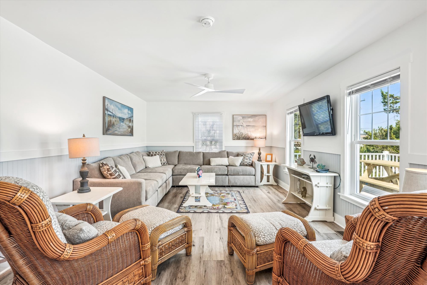 Relax in your bright living space with plush sectional seating and charming wicker chairs, where coastal artwork and warm lighting create the perfect retreat.