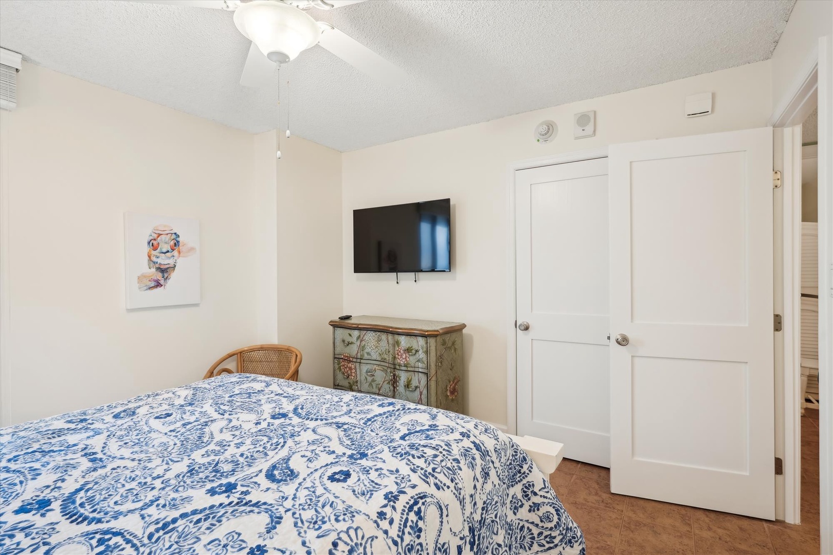 Unwind in your bright bedroom featuring a beautiful paisley-patterned bed, vintage dresser, and wall-mounted TV for cozy evening entertainment.