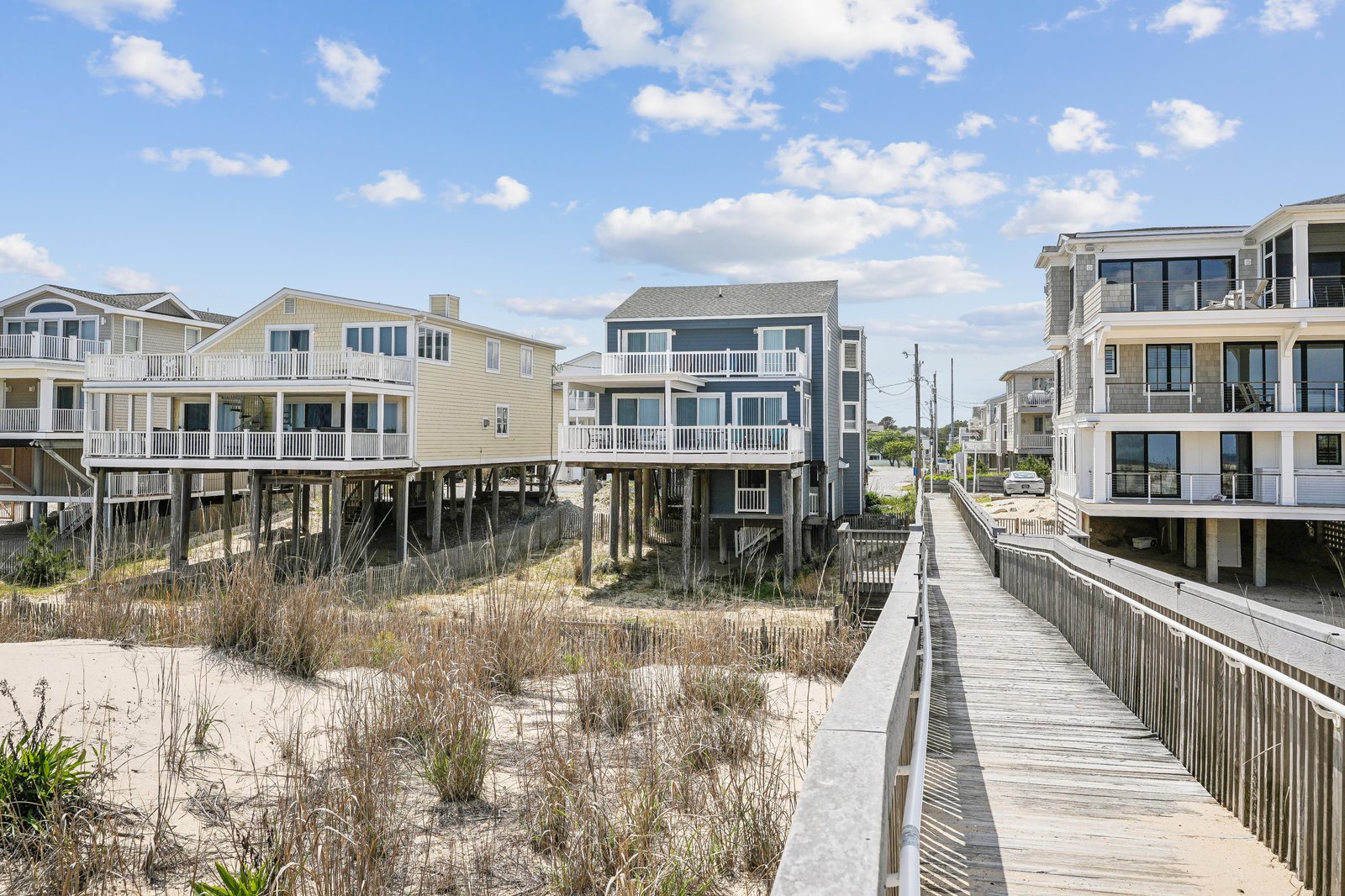 Beachfront properties line the sandy coast, offering easy access to the shore via a wooden boardwalk under clear blue skies.