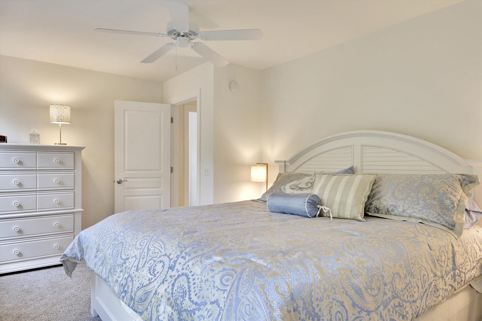 Relax in this peaceful bedroom with soft linens, gentle lighting, and a ceiling fan for your comfort.
